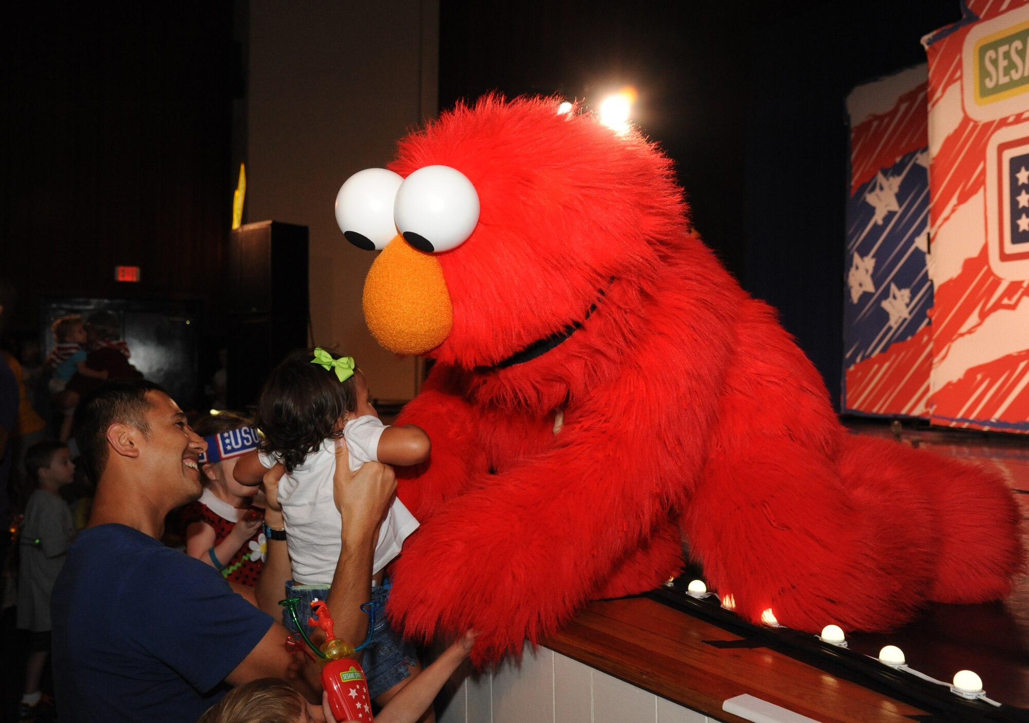 Senior Airman Dan Scheffrin, 163rd Resconnaissance Wing,  March Air Reserve Base, Calif., holds his daughter as she receives a hug from Elmo, a Sesame Street character, following a performance by Sesame Street USO Experience for Military Families show Sept. 19, 2014, at the Welch Theater, Keesler Air Force Base, Miss.  The 45-minute family-oriented event hosted by the 81st Force Support Squadron stars a character named Katie who is a military child.  With the help of her Sesame pals, Katie learns to deal with her fears and excitement about relocating.  The show emphasizes the importance of adjusting to change and the power of friendship. (U.S. Air Force photo by Kemberly Groue)