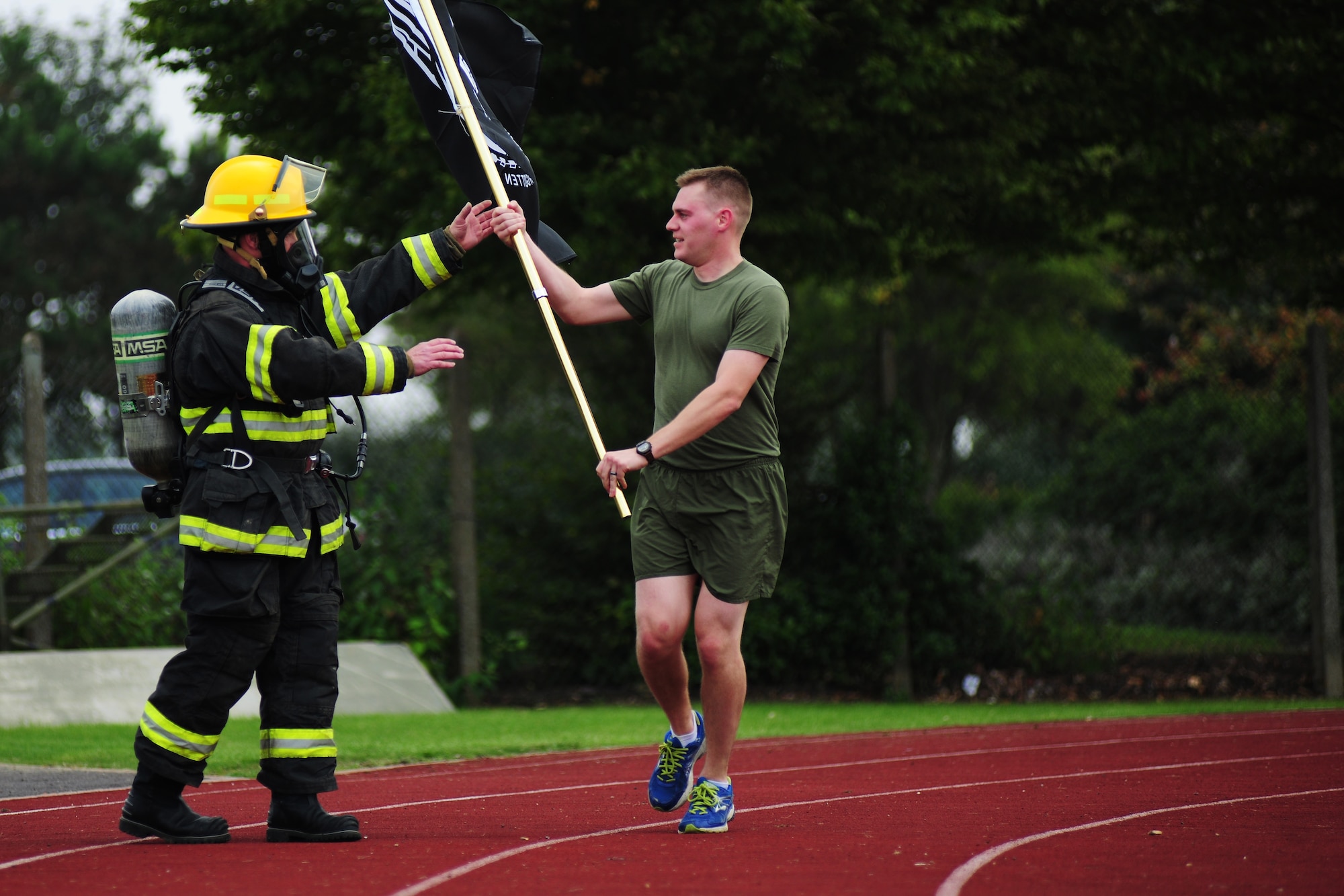 U.S. Marine Corps Staff Sgt. Kody Kromrie, U.S. Africa Command Joint Analysis Center intelligence specialist, passes the POW/MIA flag to Terry Beal, 423rd Civil Engineer Squadron fire department crew manager and Newcastle Upon Tyne, United Kingdom native, during a recognition run at RAF Alconbury, Sept. 19, 2014. The run was held as a way for Service members, civilians and British nationals to honor and remember prisoners of war and missing in action personnel. (U.S. Air Force photo by Staff Sgt. Jarad A. Denton/Released)
