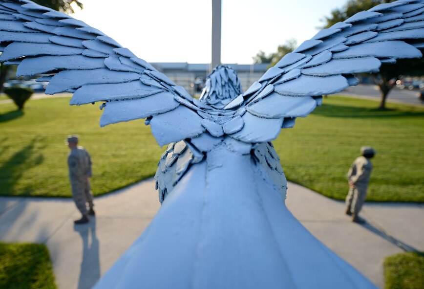 Outstretched wings of an iron eagle frame members of the 436th Airlift Wing as they stand immobile during a POW/MIA Remembrance Day vigil Sept. 19, 2014, at Dover Air Force Base, Del. The 436th AW is known as the 'Eagle Wing' and the eagle statue is hand-crafted from sheet metal over a rebar frame. (U.S. Air Force photo/Greg L. Davis)