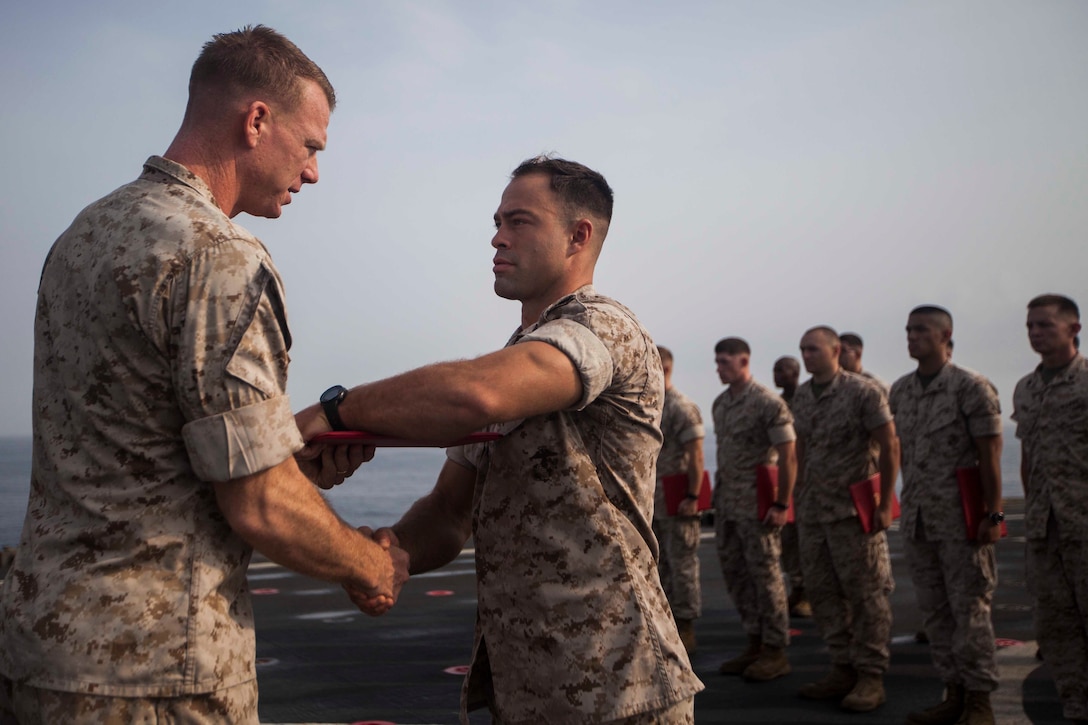 U.S. Marine Corps Cpl. Matt Blackmon, center, Battalion Landing Team 1st Battalion, 6th Marine Regiment, 22nd Marine Expeditionary Unit (MEU), fire team leader and native of Winston-Salem, N.C., receives his diploma during a corporals course graduation ceremony aboard the amphibious dock landing ship USS Gunston Hall (LSD 44). The 22nd MEU is deployed with the Bataan Amphibious Ready Group as a theater reserve and crisis response force throughout U.S. Central Command and the U.S. 5th Fleet area of responsibility. (U.S. Marine Corps photo by Sgt. Austin Hazard/Released)