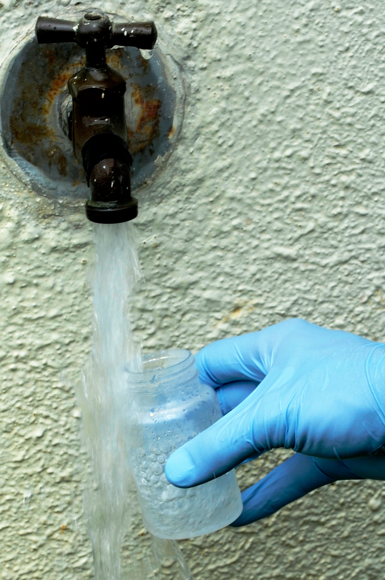 An Airman from the 18th Aerospace Medicine Squadron Bioenvironmental Engineering flight collects a water sample from a spigot on Kadena Air Base, Japan, Sept. 23, 2014. The bioenvironmental engineers conduct weekly tests of the water on base to ensure the water is safe to drink. (U.S. Air Force photo by Senior Airman Marcus Morris/Released)