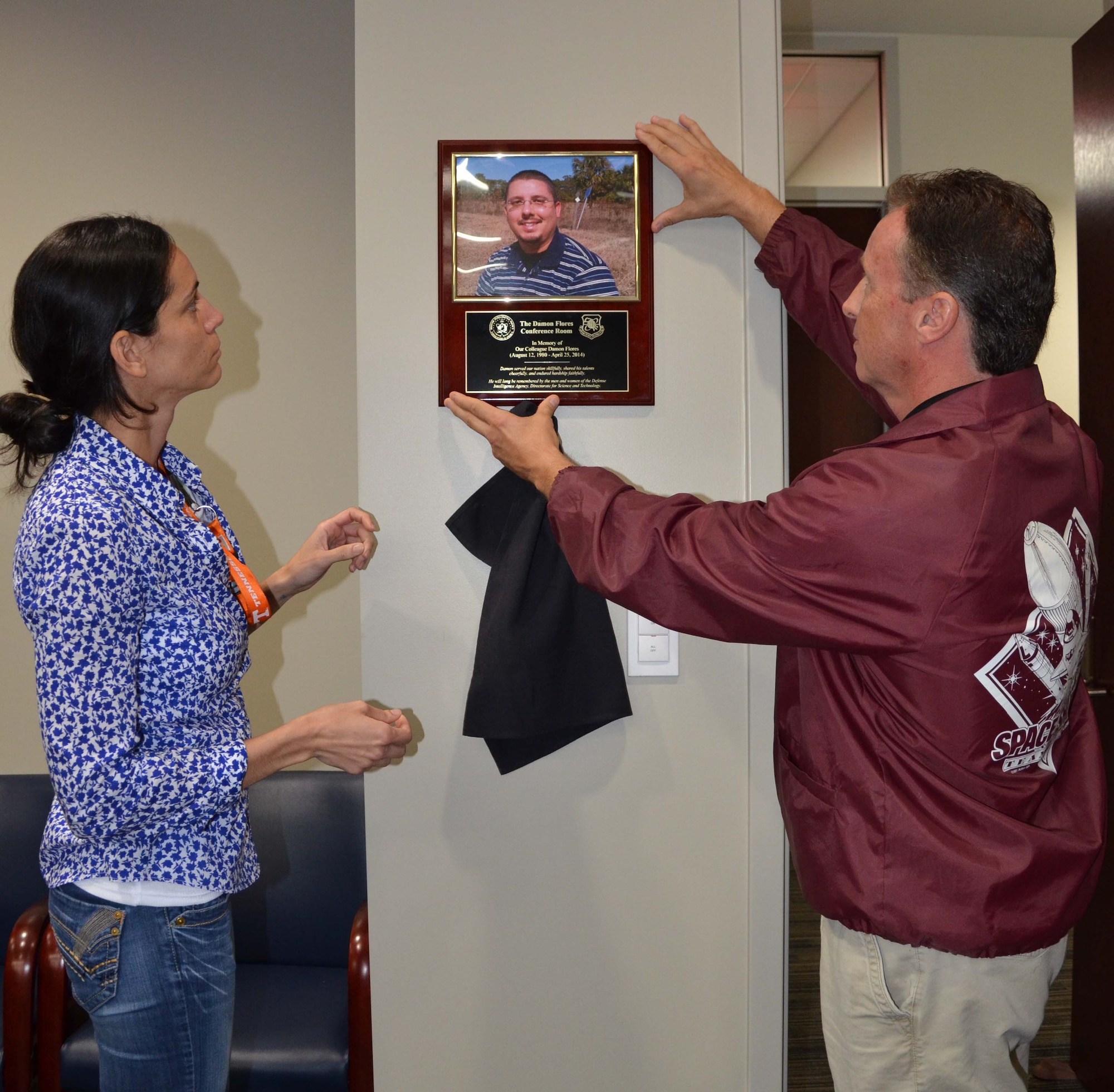 Sasha Hodge (left) and Ron Dancy, both members of the Air Force Technical Applications Center’s Operating Location-Technology Coordination, Patrick AFB, Fla., unveil a plaque dedicating their conference room to co-worker Damon Flores who passed away in April 2014.  (U.S. Air Force photo by Susan A. Romano)