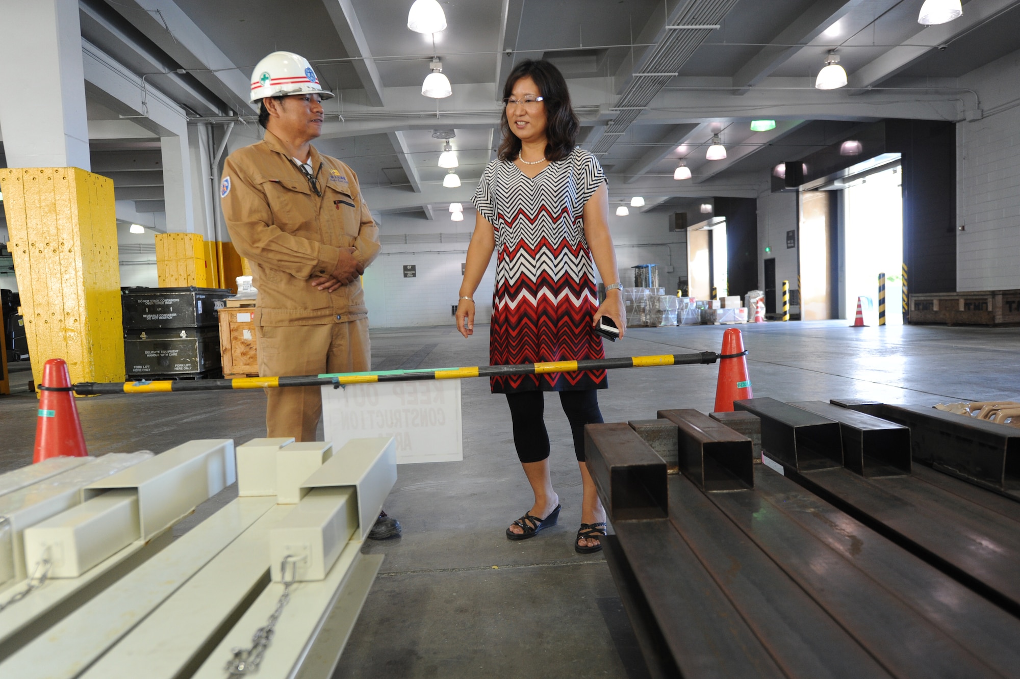 John Guadalupe, 733rd Air Mobility Squadron quality control manager (left), speaks with Keiko Okuhara, 733rd AMS facility manager (right), about reordering and replacing of the typhoon bars seen below on Kadena Air Base, Japan, Sept. 24, 2014. One of the 733rd AMS's responsibilities is the building updates to include safety such as these reinforcing bars for the roll down doors. (U.S. Air Force photo by Airmen 1st Class Zackary A. Henry/Released)