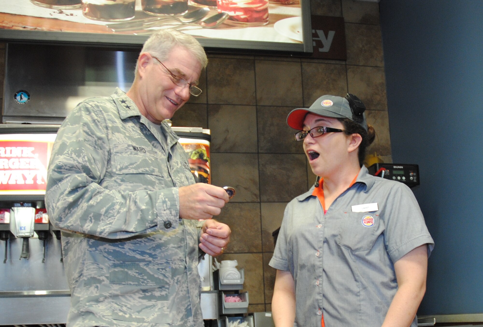 Maj. Gen. Joseph S. Ward Jr., deputy director of the Army & Air Force Exchange Service, surprises Lindsey Miracle, a Burger King assistant manager, by presenting her his challenge coin during an official visit to the Exchange on Grand Forks Air Force Base, N.D., Sept. 25, 2014. Challenge coins are presented by senior leaders in the military to military and civilian workers for excellence in job performance among other worthy reasons.  Burger King employees at the Exchange on Grand Forks AFB are considered part of the local AAFES staff. (U.S. Air Force photo/Staff Sgt. Luis Loza Gutierrez
