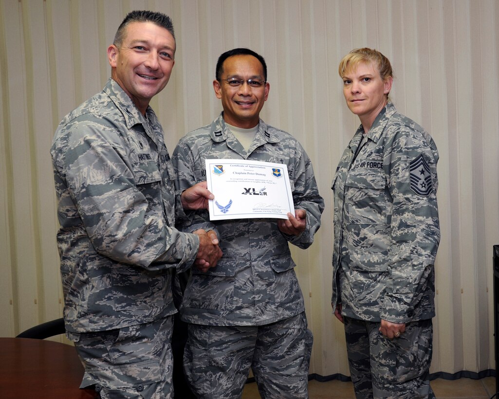 Chaplain (Capt.) Peter Dumag, center, 47th Flying Training Wing chaplain, poses with Col. Brian Hastings, left, 47th FTW commander, and Chief Master Sgt. Teresa Clapper, right, 47th FTW command chief, after being presented the XLer of the week award here Sept. 24, 2014. The XLer is a weekly award chosen by wing leadership and given to those who consistently make outstanding contributions to their unit and Laughlin. (U.S. Air Force photo by Airman 1st Class Jimmie D. Pike)(Released)