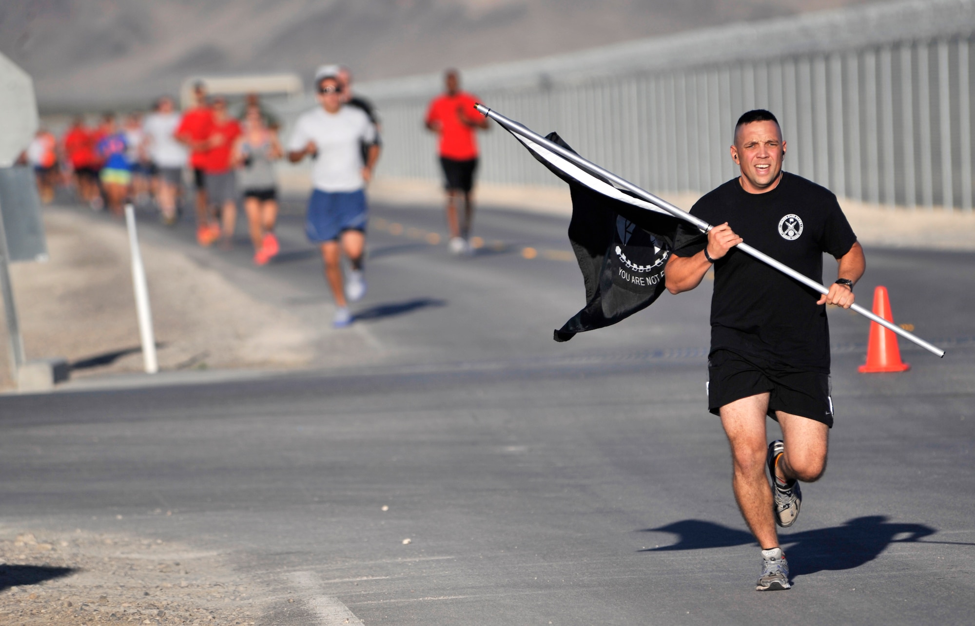 Maj. Jesse Goens, 99th Ground Combat Training Squadron commander, leads a 5K run while carrying the Prisoner of War and Missing in Action flag Sept. 17, 2014, at Creech Air Force Base, Nevada. The 5K was part of POW/MIA Remembrance Week and honored the more than 83,000 unaccounted-for U.S. servicemembers. (U.S. Air Force photo by Airman 1st Class Christian Clausen/Released)