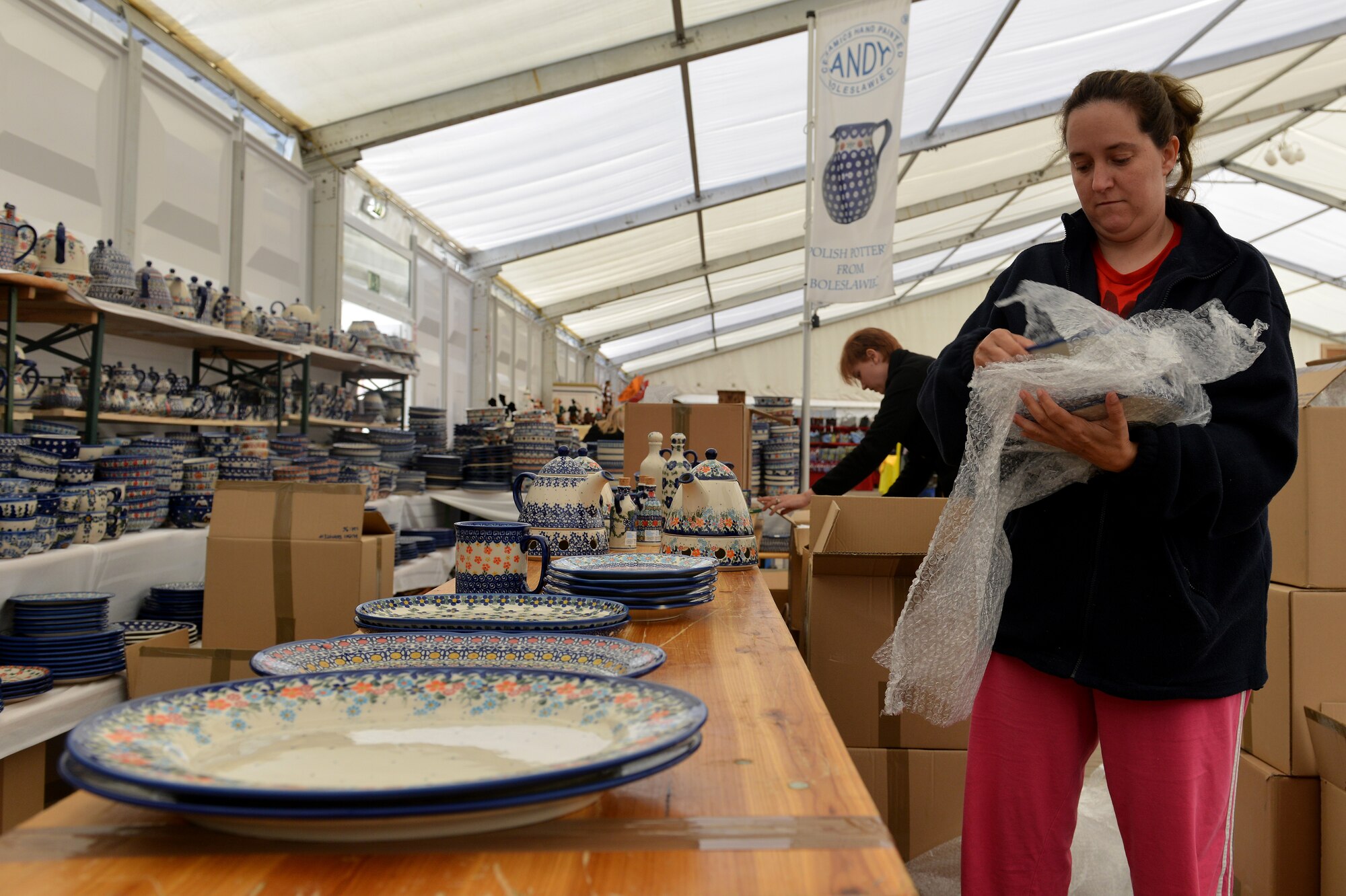 Hope Cargill and April Jones, Ramstein Welfare Bazaar volunteers, set out Polish pottery on a table on Ramstein Air Base, Germany, Sept. 20, 2014. The bazaar celebrated its 50th anniversary by hosting more than 28,000 patrons from around the Kaiserslautern Military Community and more than 160 vendors from around Europe. (U.S. Air Force photo/Senior Airman Holly Mansfield)