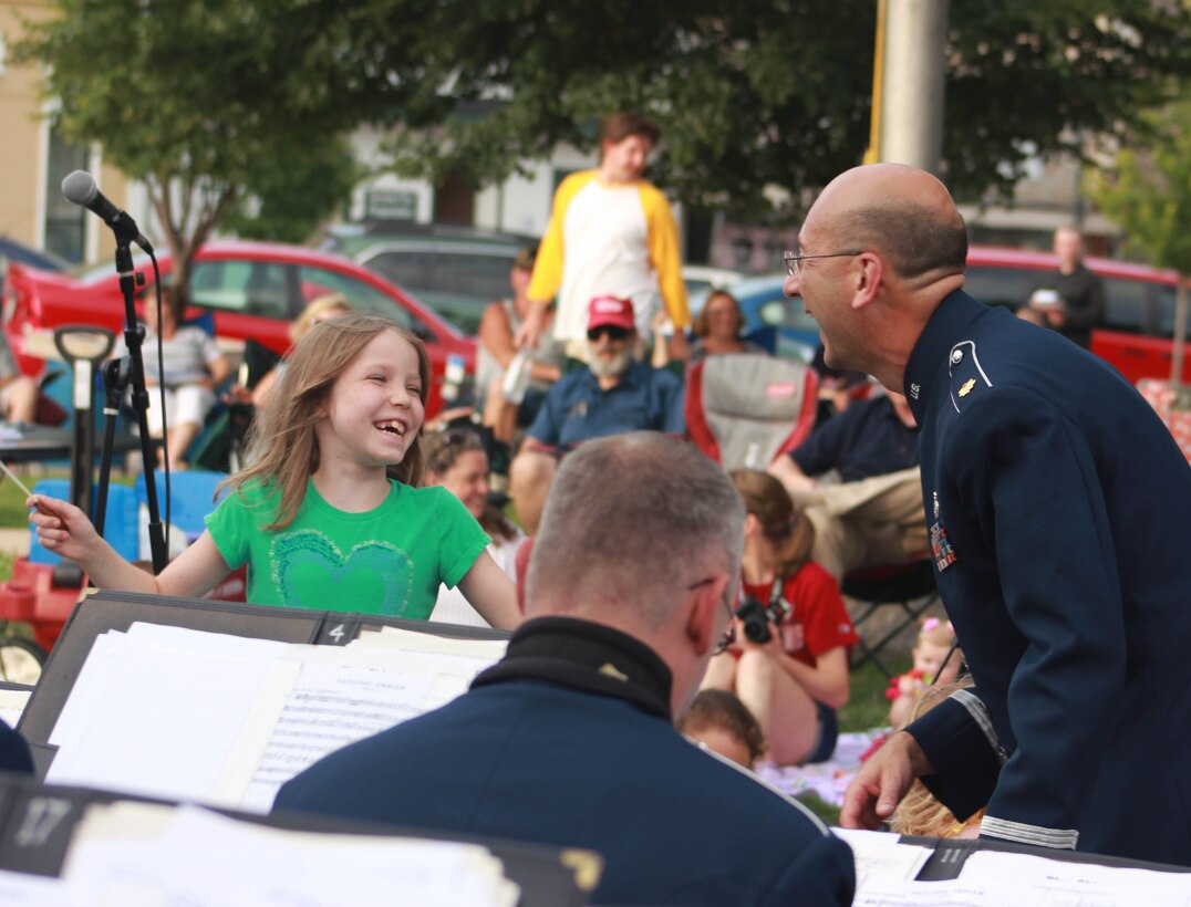 U.S. Air Force Maj. Bryan M. Miller, commander of the 566th Air Force Band, helps a girl conduct the Air National Guard Band of the Midwest while they perform for audiences during annual training at the Grundy County Courtyard Lawn, Morris, Ill., June 29, 2014. They performed jazz, rock and concert music for audiences in Illinois and Wisconsin as part of their community relations tour before a grand finale in Minnesota July 4. The annual concert series was the result of a year’s worth of training and practice, one that the band used to celebrate patriotism with communities across the Midwest. (Courtesy photo/Released)