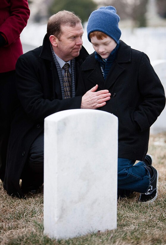 Scobee and his son, Andrew, kneel near the grave of Dick Scobee earlier this year during the NASA Day of Remembrance. Dick Scobee was the commander of the Space Shuttle Challenger, which exploded shortly after launch in 1986. His grave is near the memorials to the Space Shuttles Challenger and Columbia in Arlington National Cemetery’s Section 46.