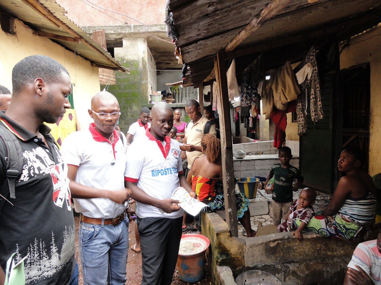 Volunteers in Guinea make their way door-to-door, sharing information about Ebola. These volunteers are able to communicate in four languages. At each dwelling, people gather to hear information about Ebola. The volunteers are wearing shirts designating their Red Cross affiliation. Centers for Disease Control and Prevention photo