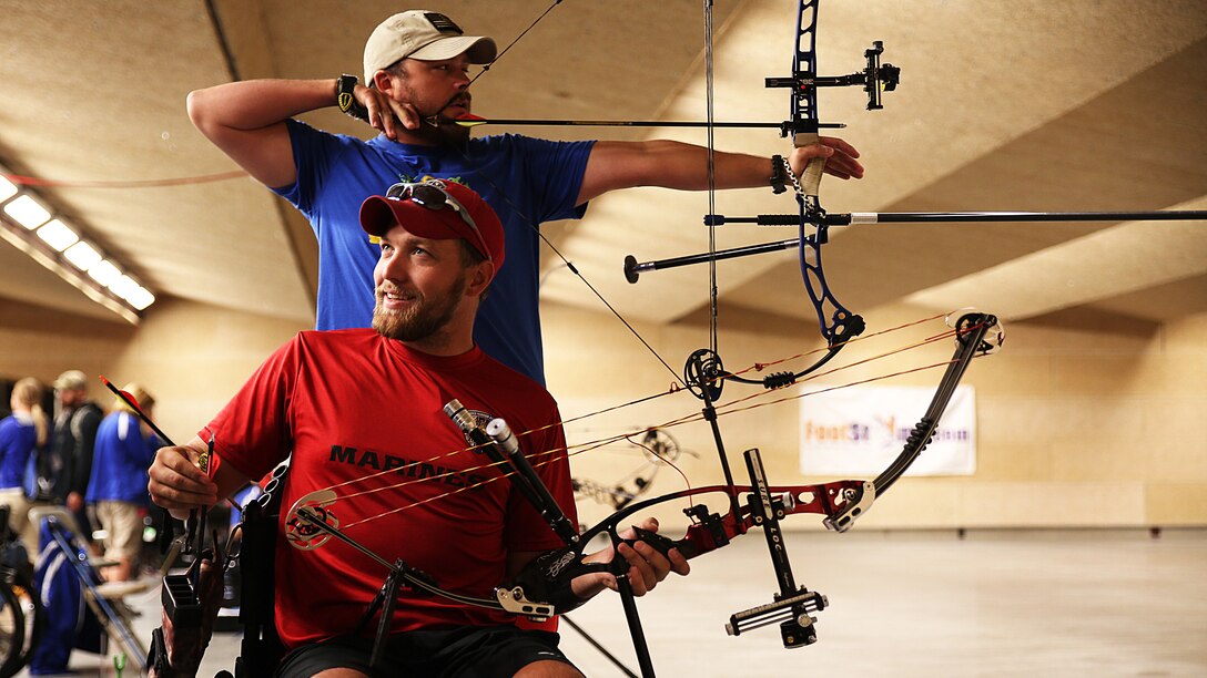 Cpl. Richard Stalder from Muenster, Texas (front) and Sgt. Clayton McDaniel from Molalla, Oregon (center) and (back) aim down range and discuss shots during archery practice for the Marine team, Sept. 24, in preparation for the 2014 Warrior Games. The Marine team has been training since September 15 in order to build team cohesion and acclimate to the above 6,000 feet altitude of Colorado Springs. The Marine team is comprised of both active duty and veteran wounded, ill and injured Marines who are attached to or supported by the Wounded Warrior Regiment, the official unit of the Marine Corps charged with providing comprehensive non-medical recovery care to wounded, ill and injured Marines. 