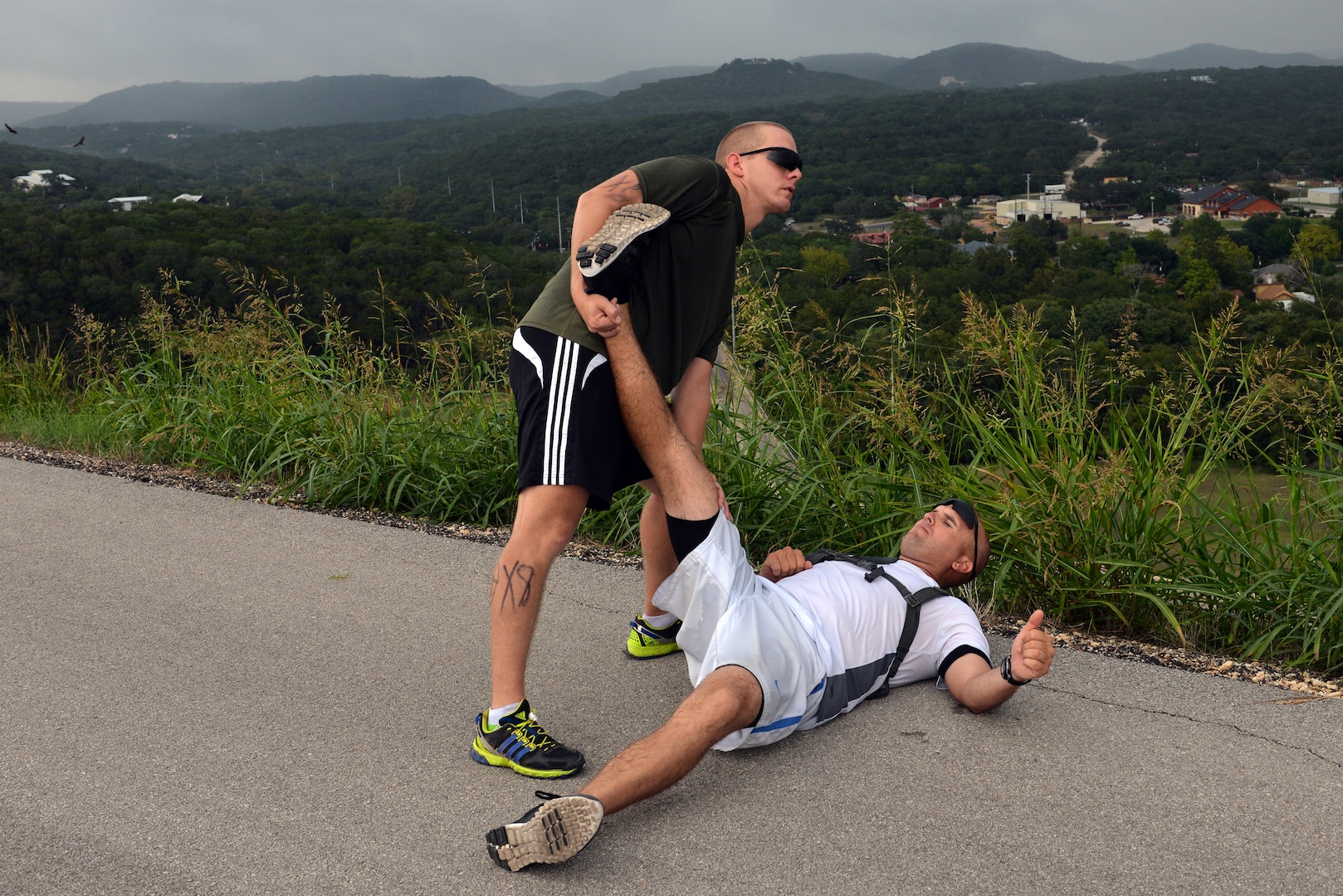 Tech. Sgt. Benjamin Funk, left, pulls Master Sgt. David Drennon’s hamstring to alleviate a muscle cramp induced by running on top of the Canyon Lake dam Sept. 20 during the Rambler 120 Race. The Rambler 120 Race, which includes running, biking, rafting and a mystery event, was held at Joint Base San Antonio Recreation Park at Canyon Lake Sept. 20. Twenty-nine teams competed in the 22-mile bike course, 6-mile run, 2-mile rafting event and a frisbee toss mystery event. Funk and Drennon are in team Beast.  (U.S. Air Force photo/Desiree N. Palacios)