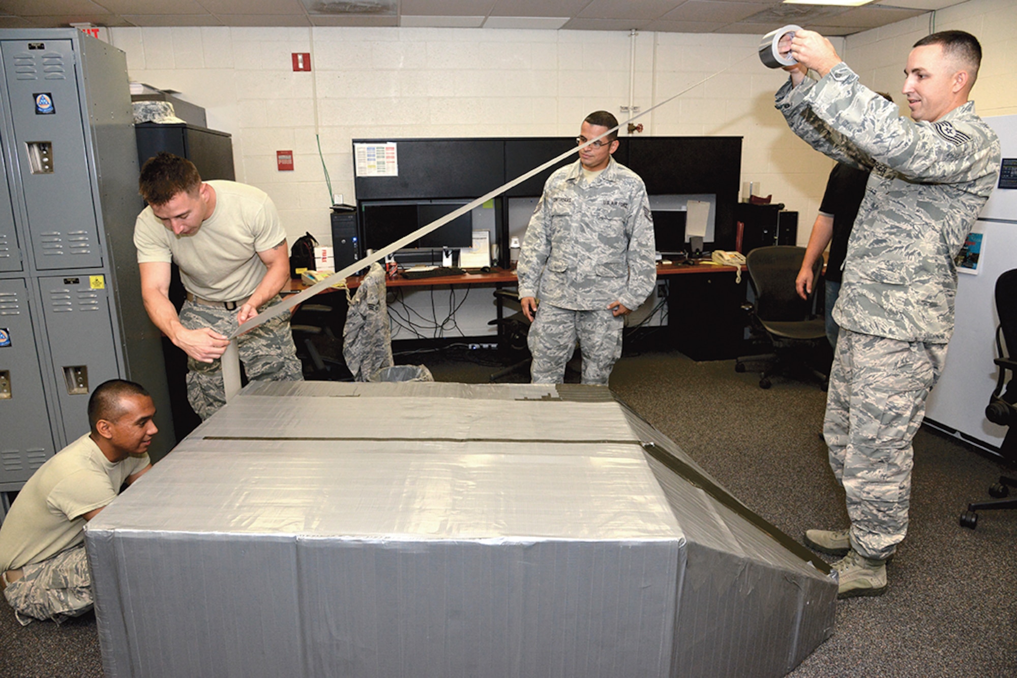 A group of Airmen reinforce their cardboard boat with massive amounts of duct  tape. The boat will be entered into the Battle of the Battleships competition Sept 26 in the indoor pool. (Photo by Ken Moore)