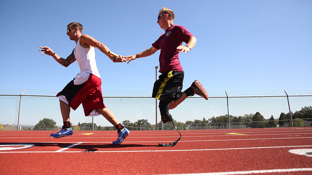 Cpl. Benjamin McCrosky (right) from Havelock, North Carolina, passes a baton to  Cpl. Sean Venezia (left) from Woodville, Mississippi, during relay track practice for the Marine team, Sept. 25, in preparation for the 2014 Warrior Games. The Marine team has been training since September 15 in order to build team cohesion and acclimate to the above 6,000 feet altitude of Colorado Springs. The Marine team is comprised of both active duty and veteran wounded, ill and injured Marines who are attached to or supported by the Wounded Warrior Regiment, the official unit of the Marine Corps charged with providing comprehensive non-medical recovery care to wounded, ill and injured Marines. The Warrior Games are a Paralympic-style competition for more than 200 wounded, ill and injured service members and are taking place Sept. 28 to Oct. 4 at the Olympic Training Center in Colorado Springs, Colorado. Follow the Marine team's progress at www.facebook.com/wwr.usmc.