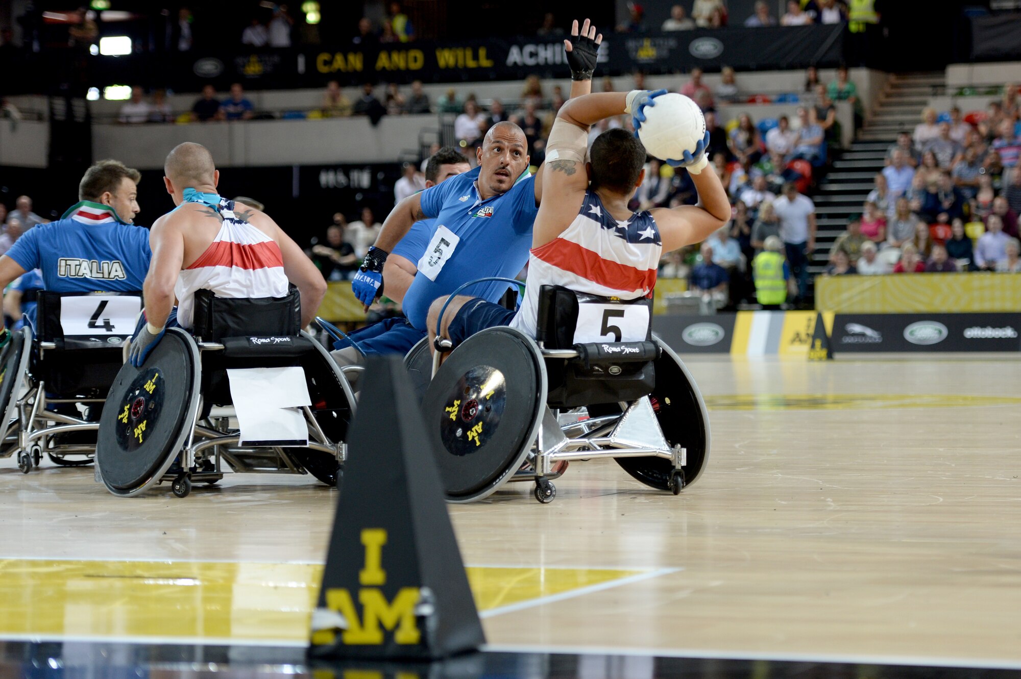 Air Force Staff Sgt. Mark Johnson passes the ball around Italy's Armondo Marco Iannuzzi during the United State's 22-4 victory over Italy in a wheelchair rugby pool match at the 2014 Invictus Games. Invictus Games is an international competition that brings together wounded, injured and ill service members in the spirit of friendly athletic competition. American Soldiers, Sailors, Airmen and Marines are representing the United States in the competition which is being held in London Sept. 10-14. (U.S. Navy photo by Mass Communication Specialist 2nd Class Joshua D. Sheppard/Released)