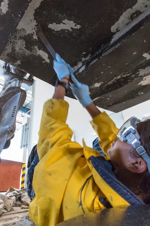 Seaman Alyza Yambo, an oil response crew member with Headquarters and Headquarters Squadron, scrapes barnacles off the bottom of a Skimmer, Sept. 29, 2014, at the Iwkauni Harbor aboard Marine Corps Air Station Iwakuni, Japan.  Excessive barnacle buildup increases the boat’s weight, causing it to use more fuel, reduce response time and reduce overall productivity.  