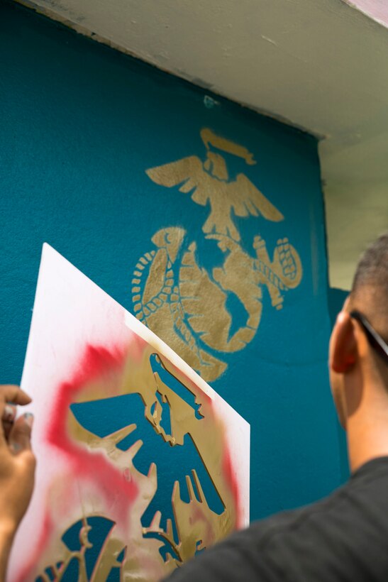 Lance Cpl. Juan Vasquez, a native of Los Angeles, California, peels a stencil off of the wall of a bus stop to reveal an Eagle, Globe and Anchor Sept. 27 in Santa Rita, Guam, as part of a volunteer project. The goal of the project was to repaint two bus stops to help beautify the local area. Vasquez, here for the Marine Corps led exercise Forager Fury III, is a ground radio repairer with Marine Tactical Air Command Squadron, Marine Air Control Group 18, 1st Marine Aircraft Wing, III Marine Expeditionary Force. (U.S. Marine Corps photo by Cpl. Lena Wakayama/Released)