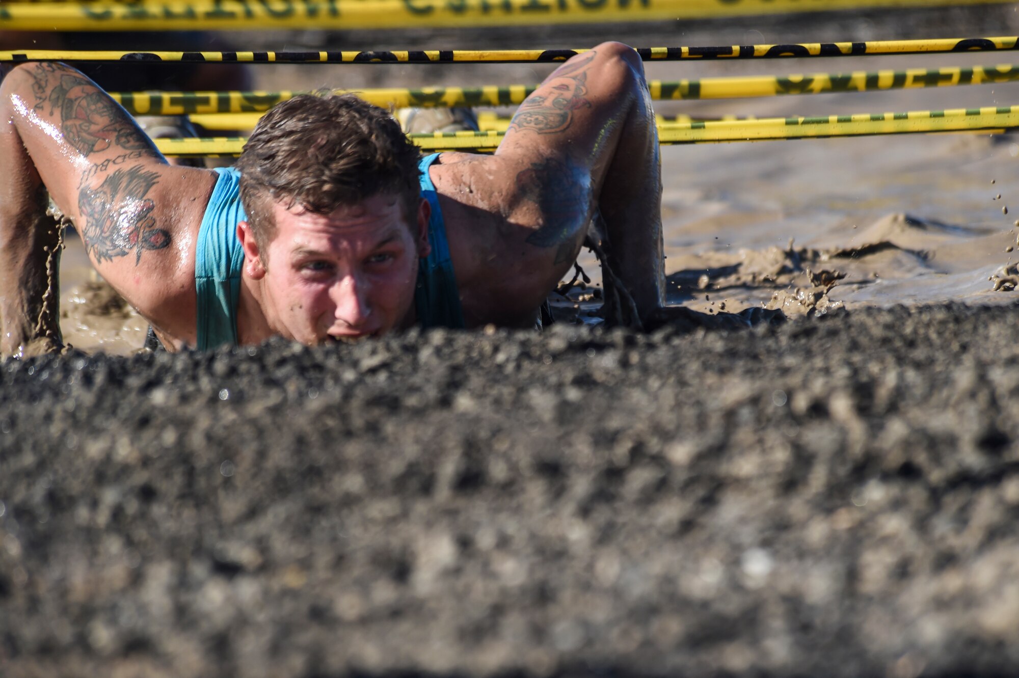 Senior Airman Lucas Maddox crawls through the mud during WARFIT Sept. 25, 2014, on Buckley Air Force Base, Colo. The 460th Civil Engineer Squadron hosted the September WARFIT, which consisted of a 5K run and a mud obstacle course. WARFIT is a way for the 460th Space Wing and base partner units to get together and stay physically fit. (U.S. Air Force photo by Senior Airman Phillip Houk/Released)