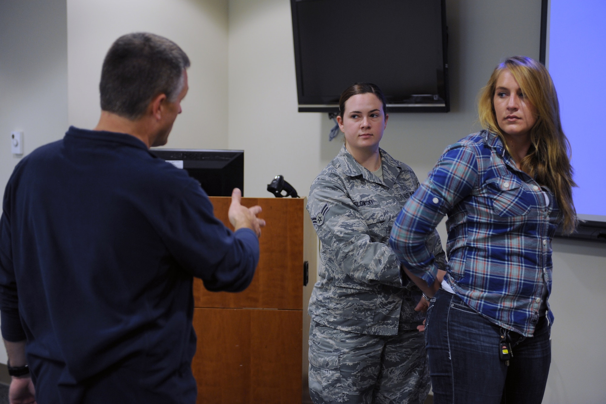 Joe Holtz (left), 375th Security Forces Squadron trainer, instructs Airman 1st Class Samantha Maslowski (center), 375th Communications Squadron, on proper hand cuffing and search techniques Sept. 24, 2014 at Scott Air Force Base, Ill. Holtz was leading a SF augmentee training session which include baton training, proper taser usage, radio procedures, hand cuffing and clothing searches. (U.S. Air Force photo/Staff Sgt. Jonathan Fowler)