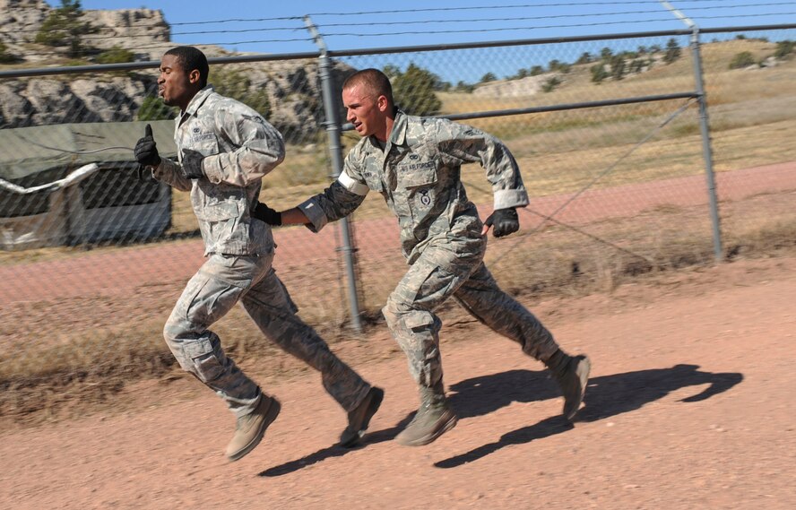 Senior Airman Kevin Swen, 5th Security Forces Squadron Global Strike Challenge team member, assists his teammate, Airman 1st Class Michael Clayton, toward the finish line during the obstacle course portion of the competition at Camp Guernsey, Wyo., Sept. 25, 2014. During the obstacle course, the team faced a number of challenges, including crawling under barbed wire and balancing on beams high above the ground. They also tested their mental skills with self-aid and buddy care and weapon assembly. (U.S. Air Force photo/Senior Airman Stephanie Morris)