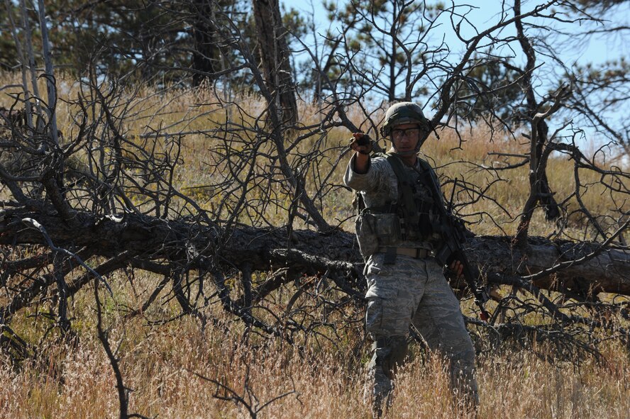 Staff Sgt. Rodrique Welton, 5th Security Forces Squadron Global Strike Challenge team member, silently communicates with his teammates during the tactics portion of the competition at Camp Guernsey, Wyo., Sept. 24, 2014. During tactics, the team navigated their way through tall ridges, billowing smoke and sharp briers to a downed helicopter surrounded by enemy guards. (U.S. Air Force photo/Senior Airman Stephanie Morris)