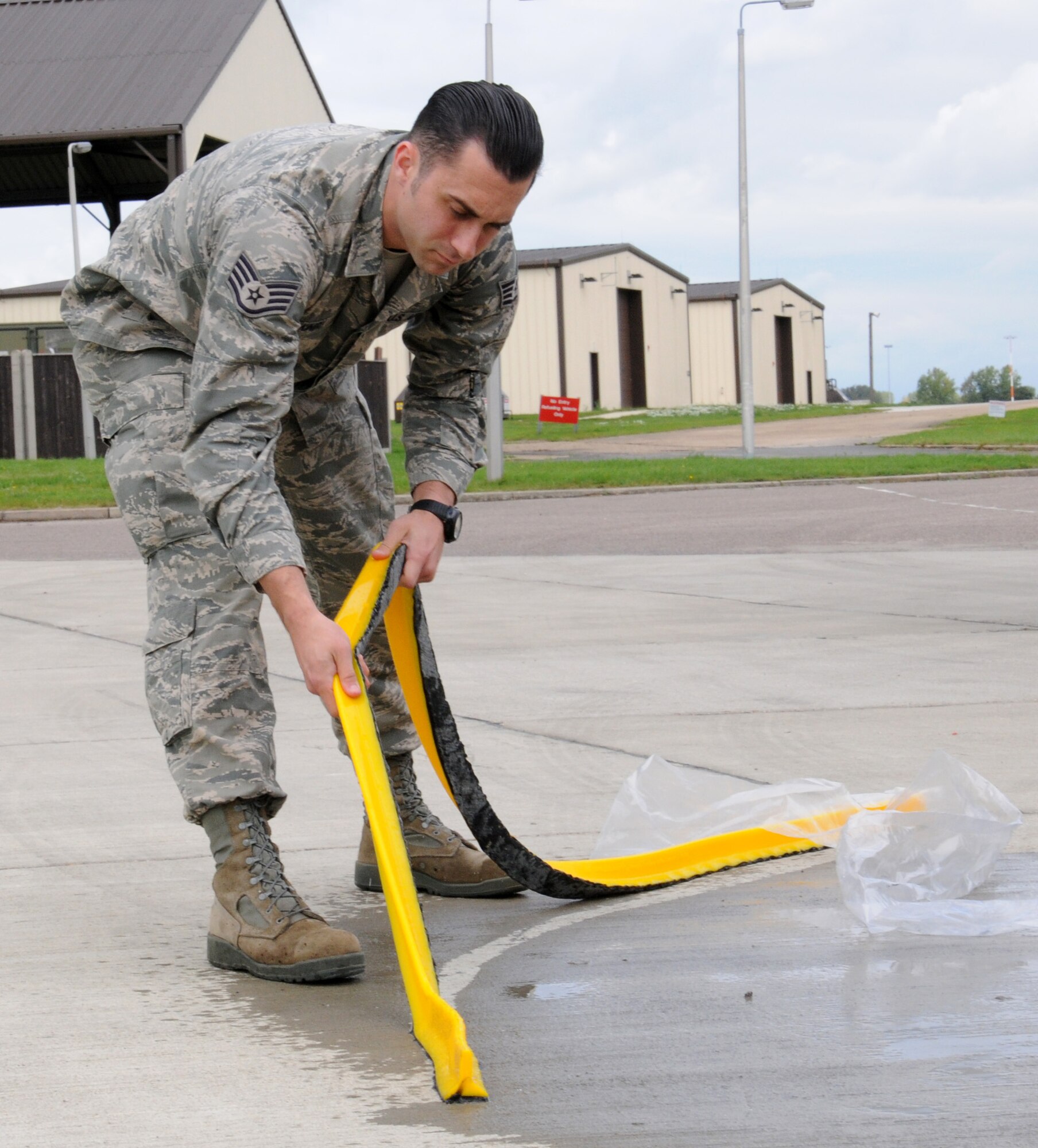 U.S. Air Force Staff Sgt. Zachary Kiniry, 100th Logistics Readiness Fuels training and support supervisor from Claremont, N.H., removes a spill dyke from the ground Sept. 24, 2014, on RAF Mildenhall, England. Kiniry developed a three-stage spill kit to contain fuel spills and prevent damage to the environment. (U.S. Air Force photo/Gina Randall/Released)