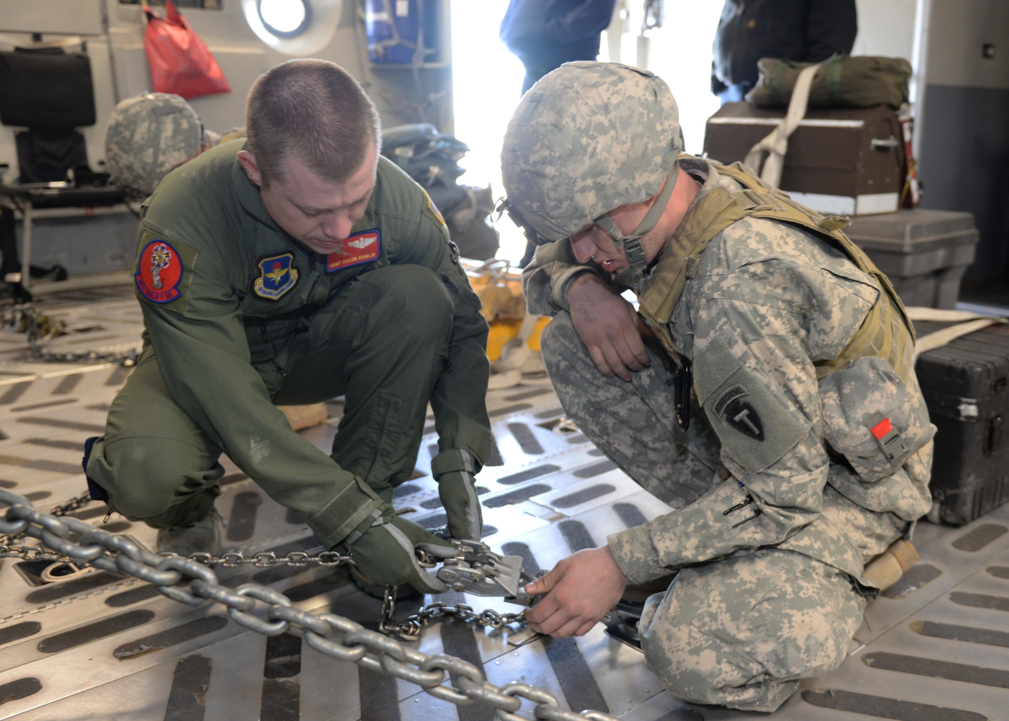 Air Force Staff Sgt. Shaun Bowlin coaches Army Spc. Matthew Crisman on tightening the cargo hold chains, ensuring the cargo is secured properly on an Air Force C-17 Globemaster III March 27, 2015, at Perrin Airfield, Texas. The aircrew from Altus Air Force Base, Oklahoma, met with Soldiers from the 1st Battalion (Airborne), 143rd Infantry Regiment, for a joint-force exercise. Bowlin is a loadmaster assigned to the 58th Airlift Squadron and Crisman is an infantryman assigned to the 143rd IR. (U.S. Air Force photo/Senior Airman J. Zuriel Lee)