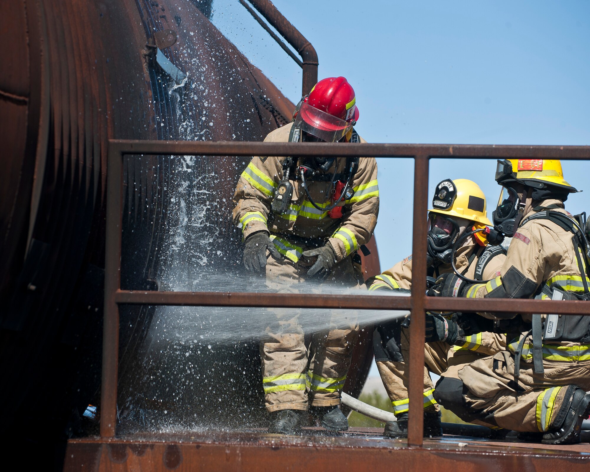 Firefighters from the Merced County Fire Department’s Castle Fire Station 62, Atwater, Calif., spray water on an aircraft’s door prior to breaching it during training at the burn pit on Nellis Air Force Base, Nev., March 27, 2015. Water was sprayed on the door as a precaution because fire was raging on the other side. (U.S. Air Force photo by Staff Sgt. Siuta B. Ika)