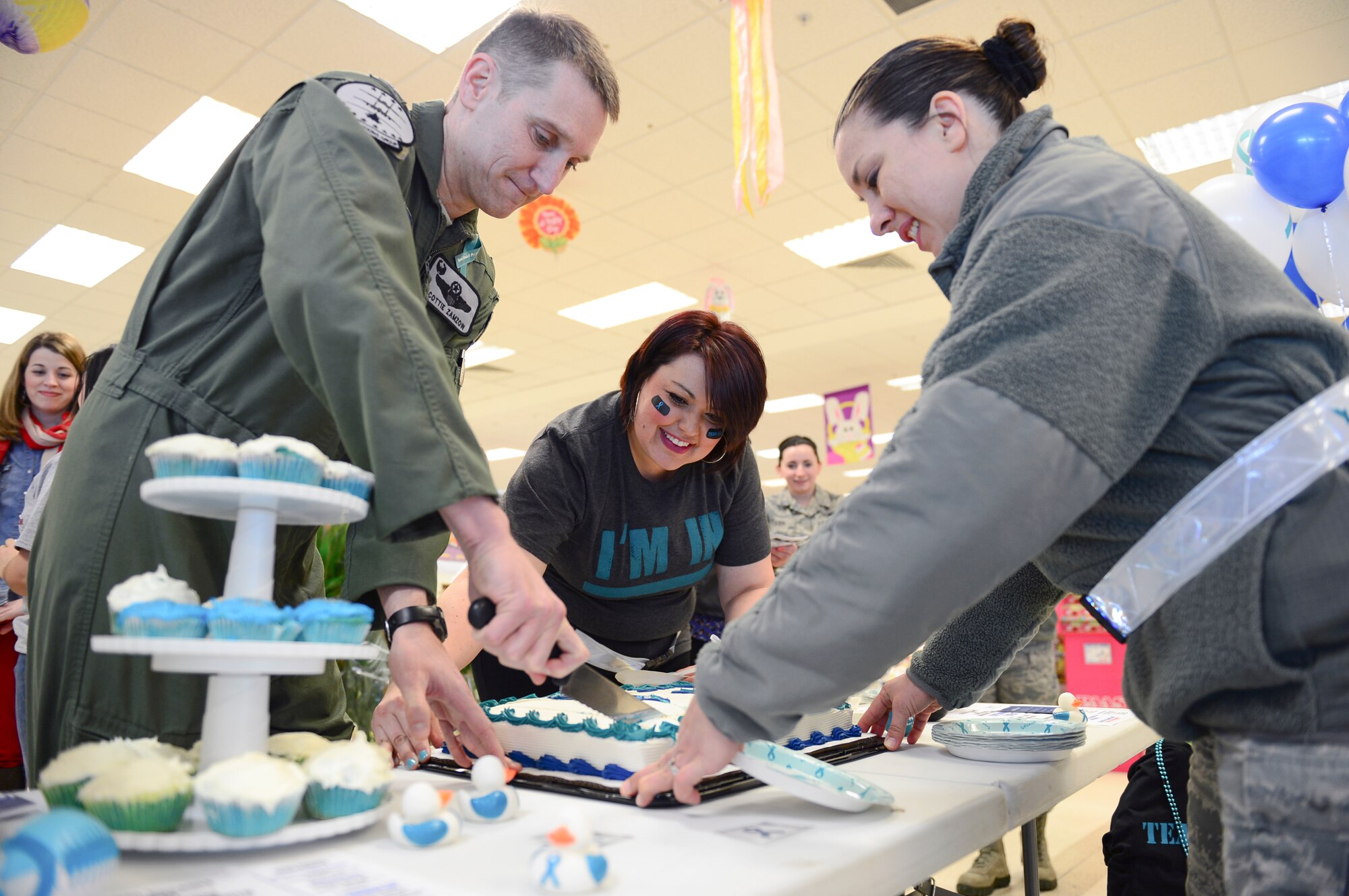 Col. Scottie Zamzow, 48th Operations Group commander, and Carolina Yepez, 48th Fighter Wing Sexual Assault Response Coordinator, pass out cake at the commissary on Royal Air Force Lakenheath, England, April 1, 2015. The Sexual Assault Prevention and Response team and the Family Advocacy program hosted the kick-off event for Sexual Assault and Child Abuse Awareness Month. (U.S. Air Force photo by Airman 1st Class Dawn M. Weber/Released)