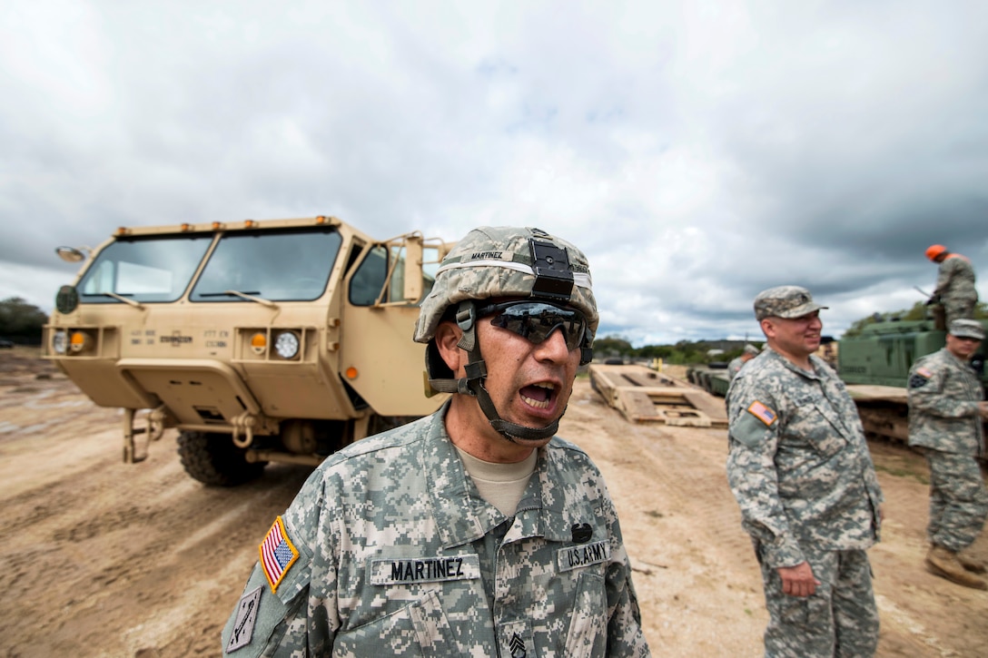 Army Staff Sgt. Raul Martinez, foreground, calls out to other soldiers while staging vehicles on Camp Bullis, Texas, March 22, 2015. Martinez is a squad leader assigned to the 277th Engineer Company.