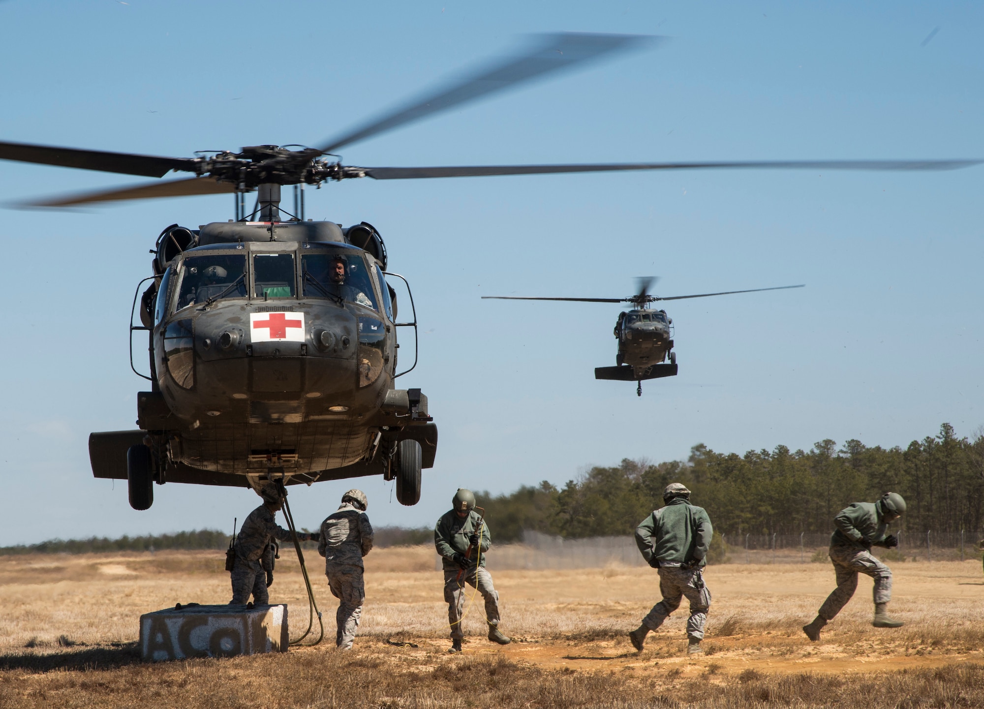 Airmen from the 621st Contingency Response Wing run away from a U.S. Army UH-60 Black Hawk helicopter assigned to the 1-150th Assault Helicopter Battalion after hooking up cargo, as another Black Hawk waits for its turn during sling-load training at Joint Base McGuire-Dix-Lakehurst, N.J., April 1, 2015. The training allows the Army pilots and crew members and Air Force Airmen to stay proficient with sling-load operations. (U.S. Air Force photo/Staff Sgt. Gustavo Gonzalez/RELEASED)