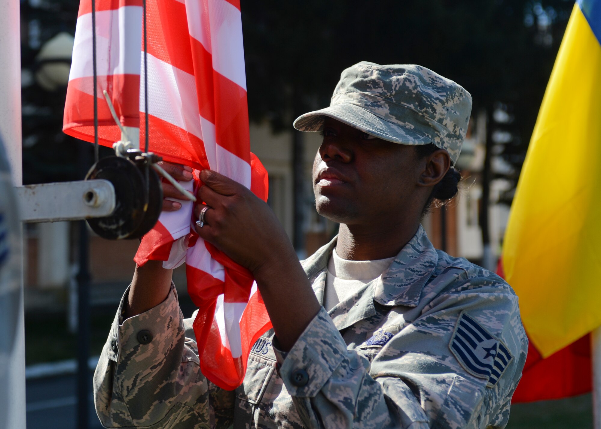 U.S. Air Force Tech. Sgt. Fallon Cornelius, a client systems technician assigned to the 354th Expeditionary Fighter Squadron, unfurls an American flag during the opening ceremony of Dacian Thunder 2015 at Campia Turzii, Romania, April 1, 2015. Cornelius and 300 fellow Airmen and support equipment from the 355th Fighter Wing at Davis-Monthan Air Force Base, Arizona, and the 52nd Fighter Wing at Spangdahlem Air Base, Germany, will support the theater security package as part of Operation Atlantic Resolve. (U.S. Air Force photo by Staff Sgt. Joe W. McFadden/Released)