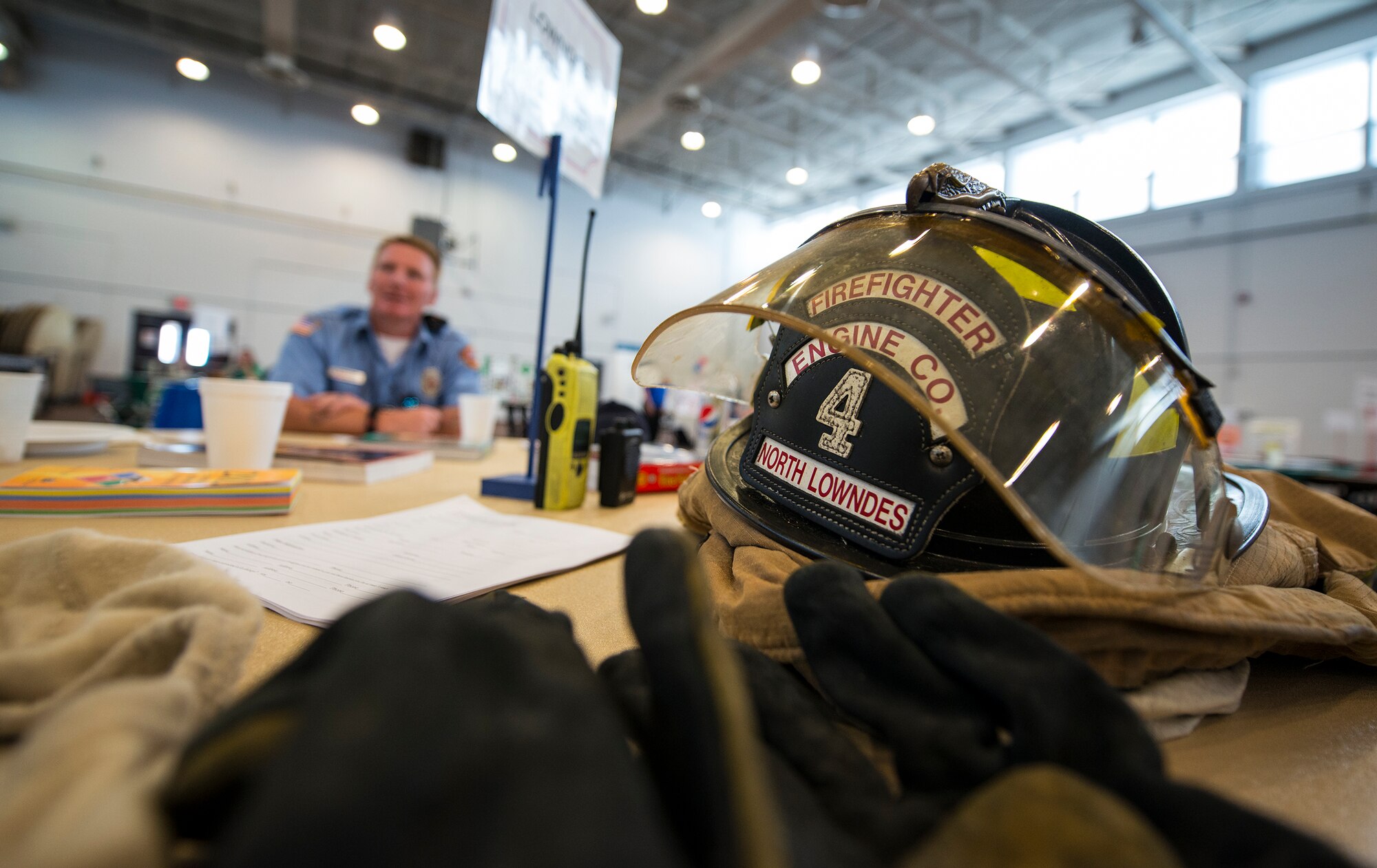 Firefighter bunker gear rests on a table while Mark White Eagle, local volunteer firefighter, explains the duties and responsibilities of being a volunteer firefighter during the Volunteer Fair April 1, 2015, at Moody Air Force Base, Ga. The various organizations provide flexible volunteer hours to accommodate different work schedules. (U.S. Air Force photo by Airman 1st Class Ceaira Tinsley/Released)