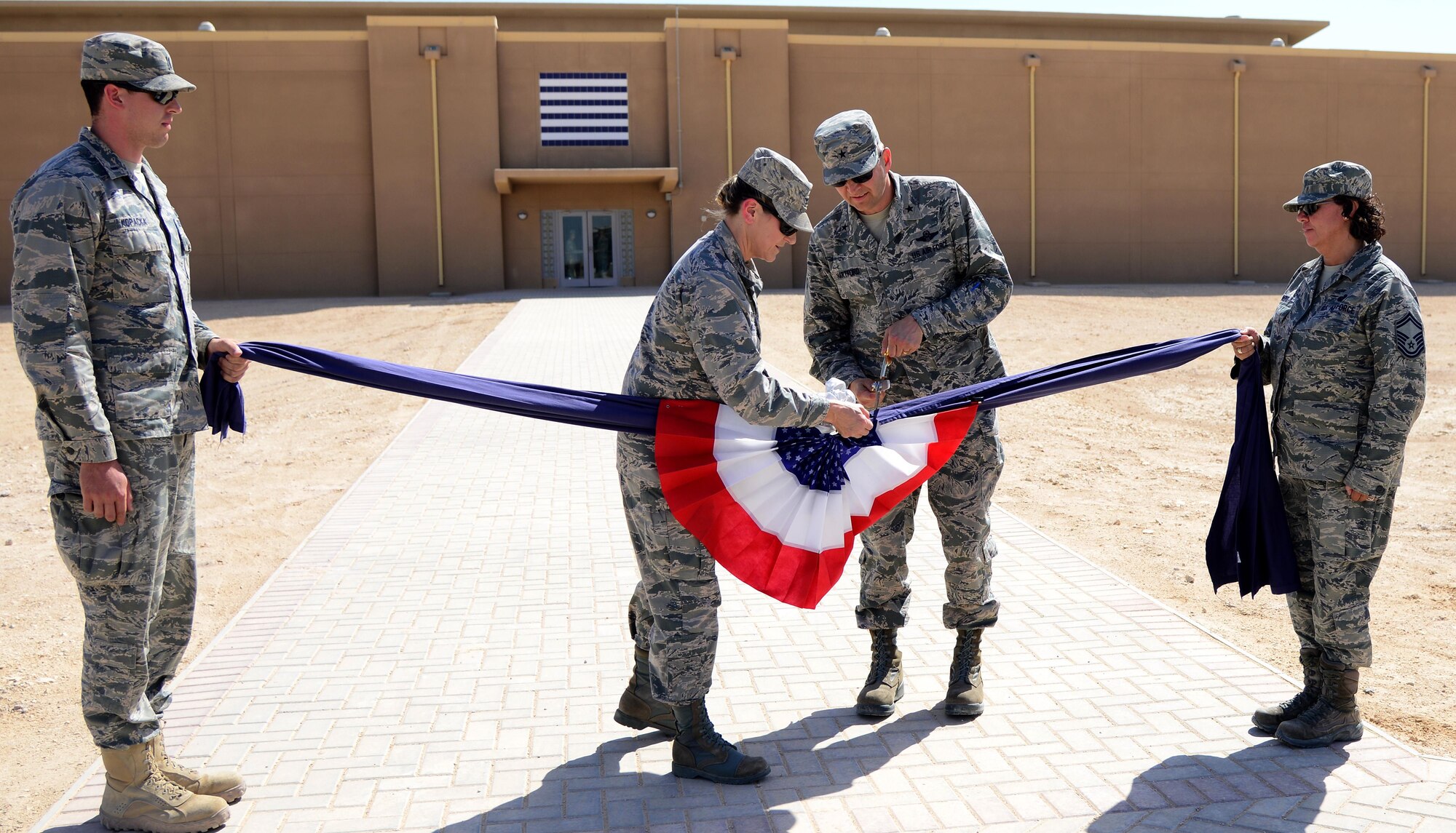 U.S. Air Force Col. Caroline Miller, 379th Expeditionary Mission Support Group commander, and Brig. Gen. Darren Hartford, 379th Air Expeditionary Wing commander, cut the ceremonial linen during a linen cutting ceremony, April 3, 2015, at Al Udeid Air Base, Qatar. The linen cutting ceremony symbolized the opening of the new Phase II dormitories in the Blatchford-Preston Complex. (U.S. Air Force photo by Senior Airman Kia Atkins)