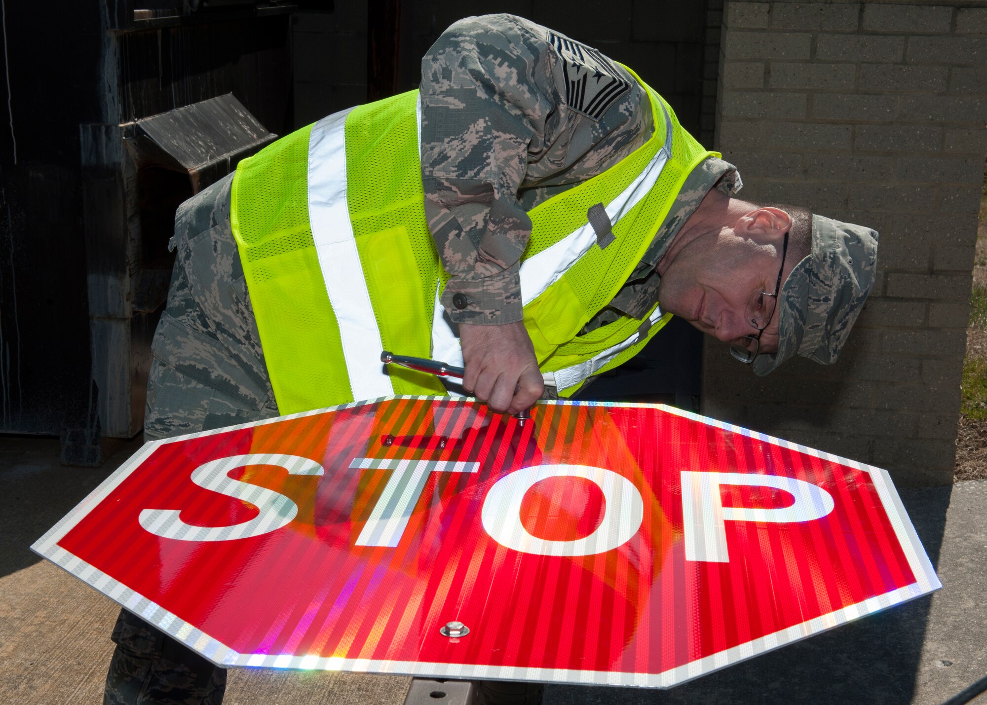 Chief Master Sgt. Stanley Cadell, 436th Airlift Wing command chief, attaches a new stop sign to its pole April 1, 2015, at Dover Air Force Base, Del. Cadell assembled this new “break-away” stop sign, which meets Air Force safety compliances. (U.S. Air Force photo/Airman 1st Class Zachary Cacicia)