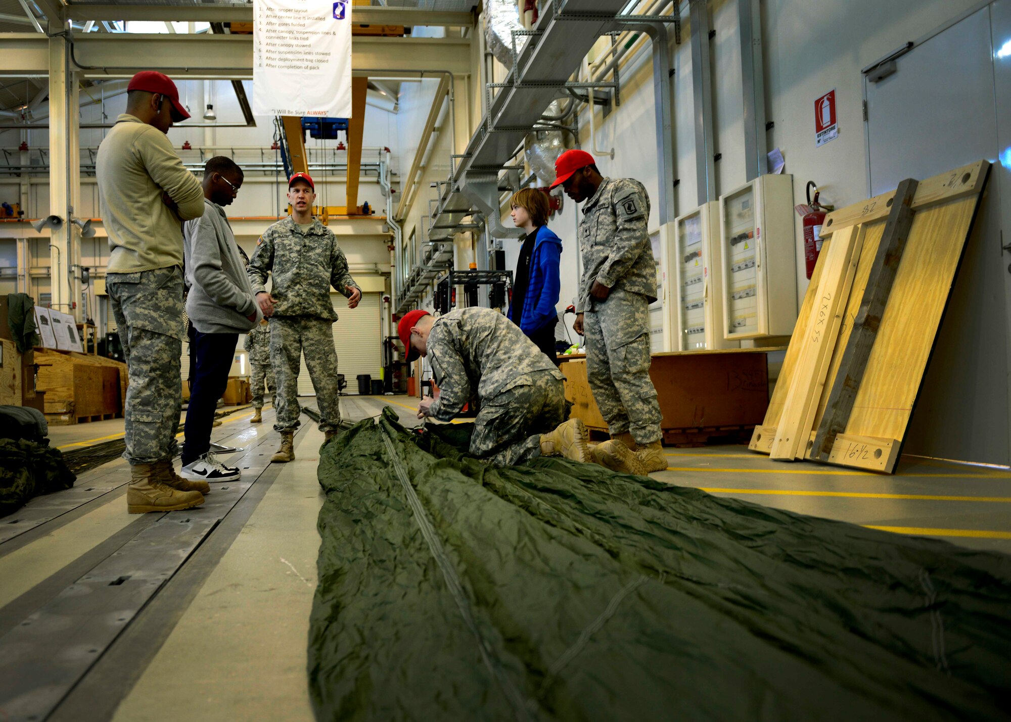 U.S. Army parachute riggers show Aviano Middle/High School students a heavy equipment parachute during job shadow day, April 2, 2015, at Aviano Air Base, Italy. Throughout their visit to the Headquarters and Headquarters Company 173rd Brigade Support Battalion, students gained hands on, parachute packing experience. (U.S. Air Force photo by Senior Airman Areca T. Wilson/Released)