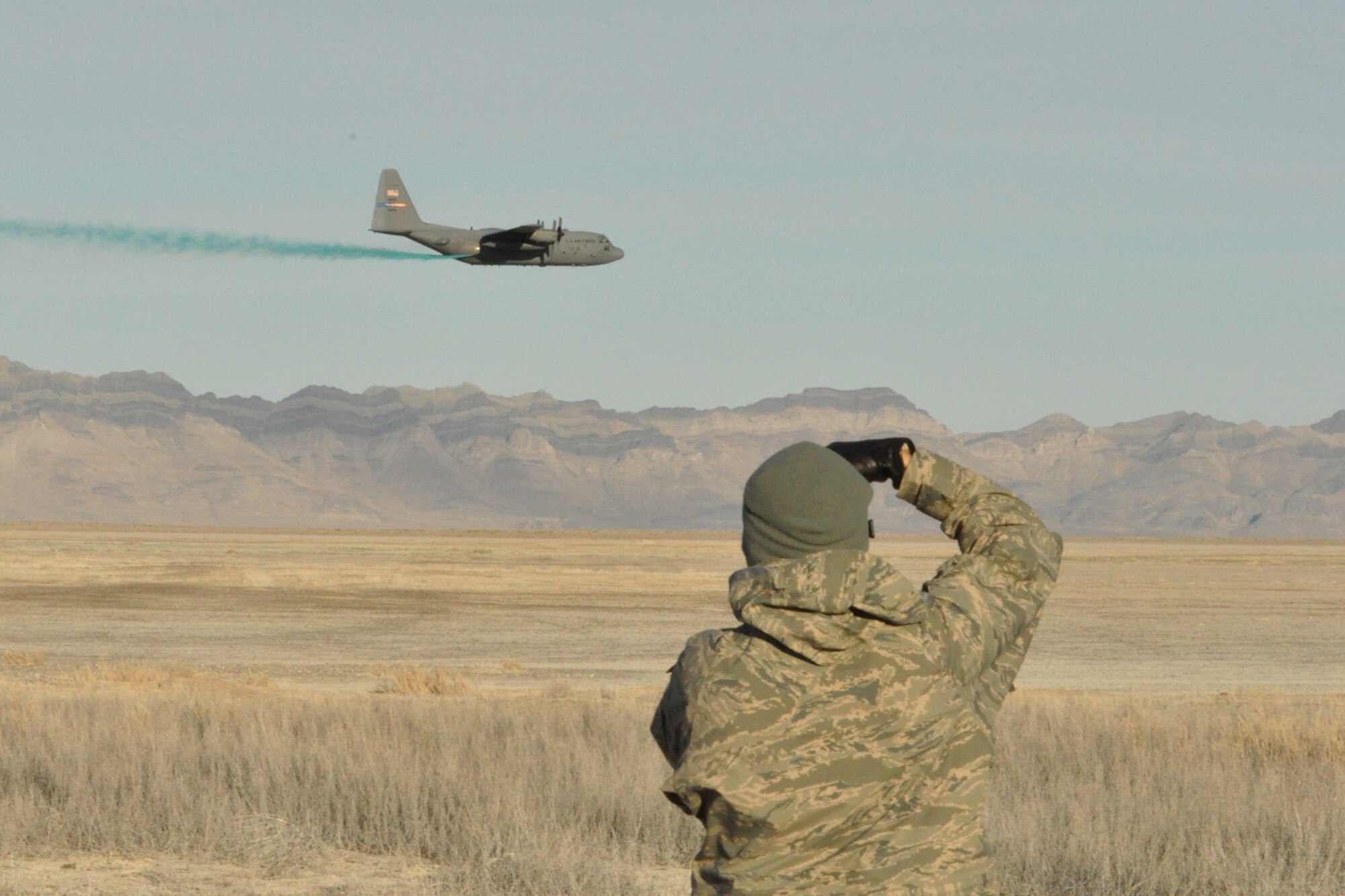 Air Force Reserve Tech. Sgt. Rick Lisum, 910th Airlift Wing Public Affairs Photojournalist based at Youngstown Air Reserve Station, Ohio, photographs a C-130 Hercules aircraft conducting aerial spray operations at an altitude of approximately 100 feet above the ground over a target site on the Utah Test and Training Range nearby here, March 18, 2015. The C-130 assigned to 910th Airlift Wing based at Youngstown Air Reserve Station, Ohio and home to the Department of Defense’s only large area, fixed wing aerial spray capability, is flying at the low altitude to control the placement of herbicide onto the selected target areas while conducting a two-week aerial spray mission over UTTR, March 9 – 20, 2015, to eliminate unwanted ground-covering invasive weeds. 
