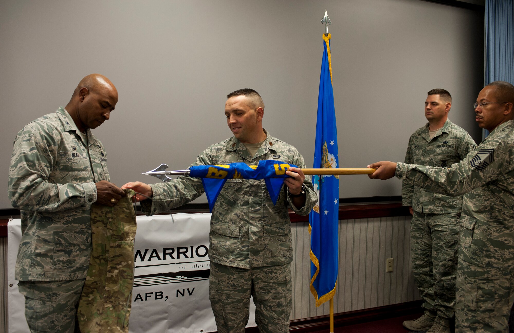Col. Richard Neal, 799th Air Base Group commander, and Maj. Jesse Goens, 99th Ground Combat Training Squadron commander, prepare to place a cover over the 99th GCTS guidon, officially inactivating the 99th GCTS, at Nellis Air Force Base, Nev., April 1, 2015. Before inactivating, the 99th GCTS received the first Air Combat Command Security Forces Order of the Shield unit awar Feb. 6, 2015. The 99th GCTS was responsible for conducting training on Silver Flag Alpha, where Airmen taught and evaluated security forces members on air base defense skills. (U.S. Air Force photo by Airman 1st Class Jake Carter)