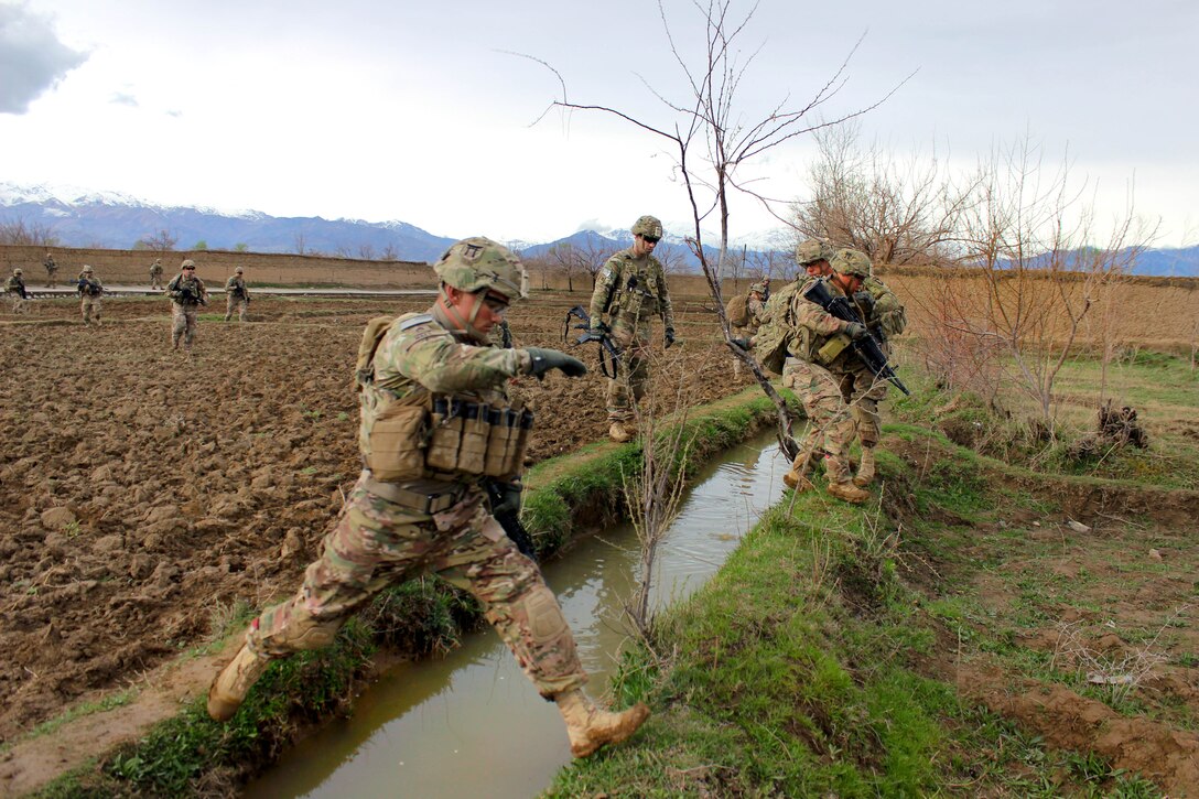 U.S. soldiers leap over a canal after patrolling through a field near Bagram Airfield, Afghanistan, March 24, 2015.