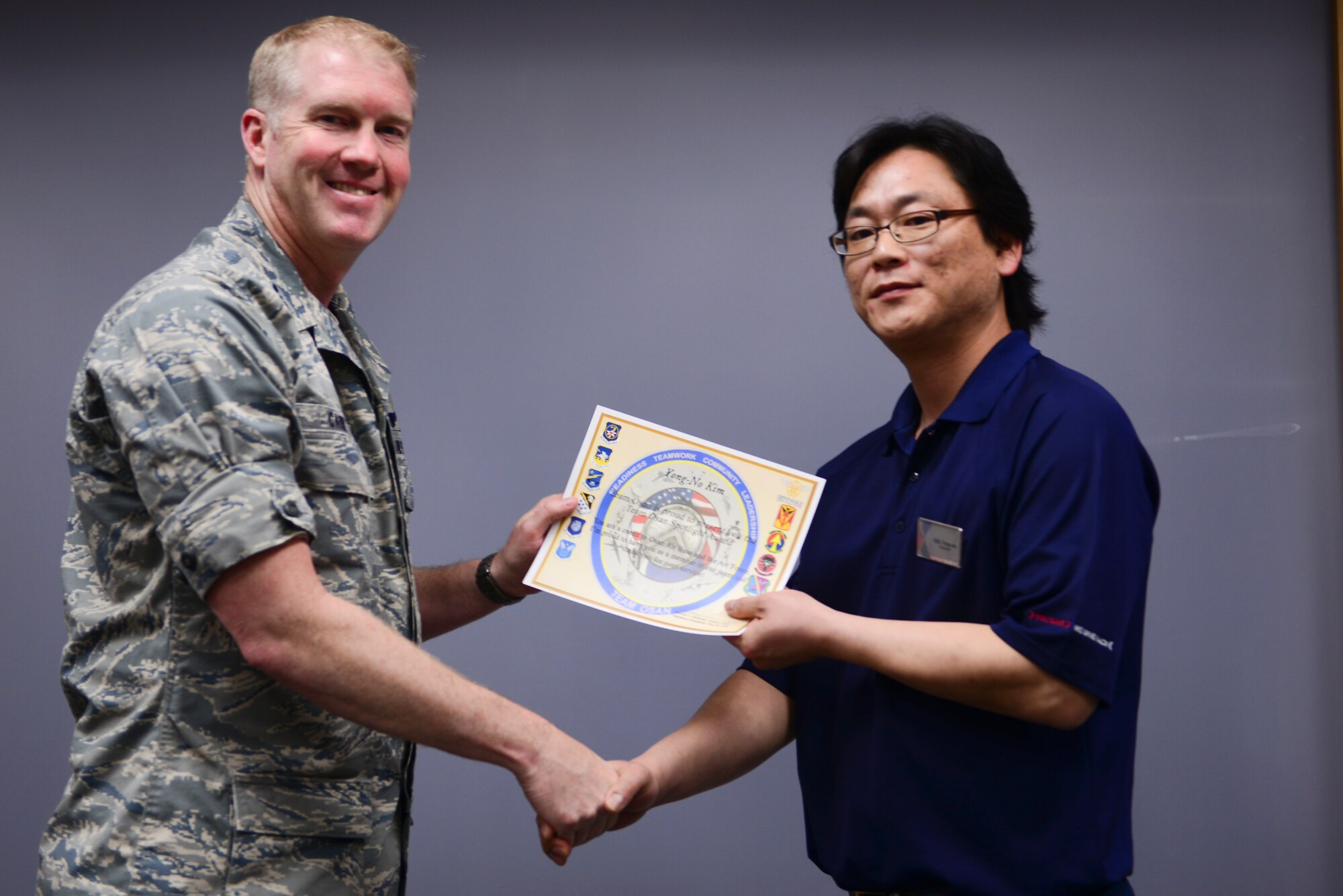 Col. Brain Carr, 51st Fighter Wing vice commander, presents Mr. Yong-No Kim, Army and Air Force Exchange Service electronics supervisor, a spotlight certificate April 7, 2015, at Osan Air Base, Republic of Korea. Mr. Kim has worked for AAFES since 2000. (U.S. Air Force photo by Staff Sgt. Benjamin Sutton/Released)