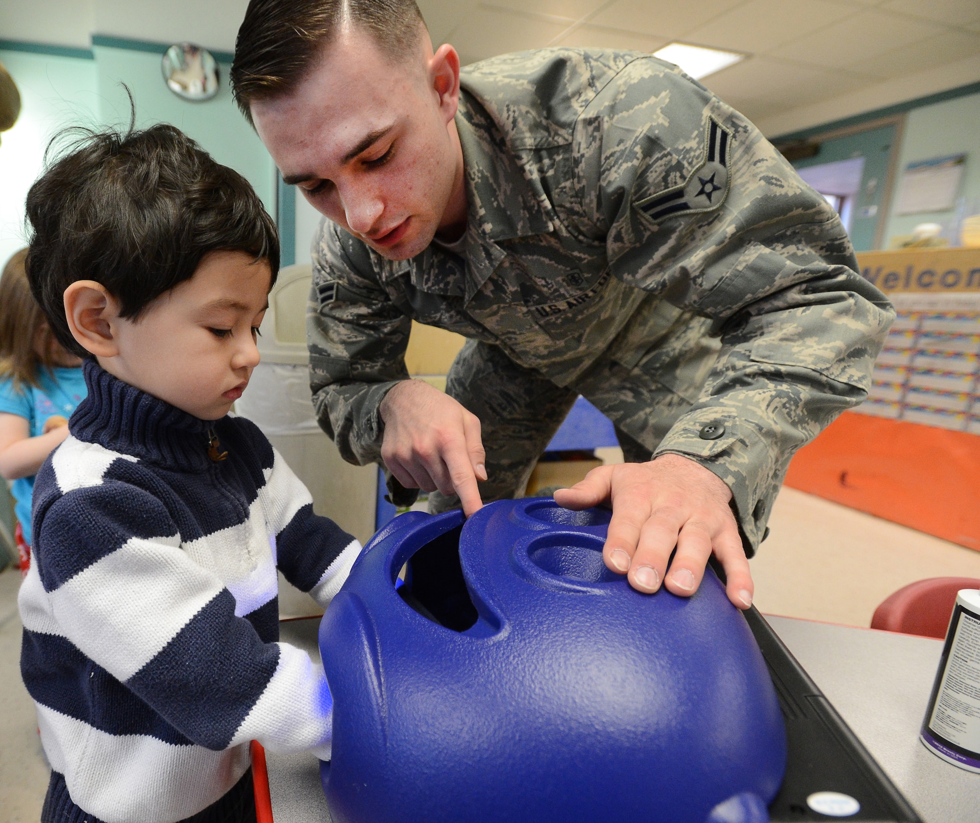 Airman 1st Class Jordan Phillips, 66th Medical Squadron Public Health technician, has Eli Proschitsky place his hands in a Glitter Bug during a hygiene lesson as part of a National Public Health Week event at the Child Development Center, Apr. 7. Public Health members used this lesson as a way to show children how effective washing hands are in removing germs. (U.S. Air Force photo by Jerry Saslav)