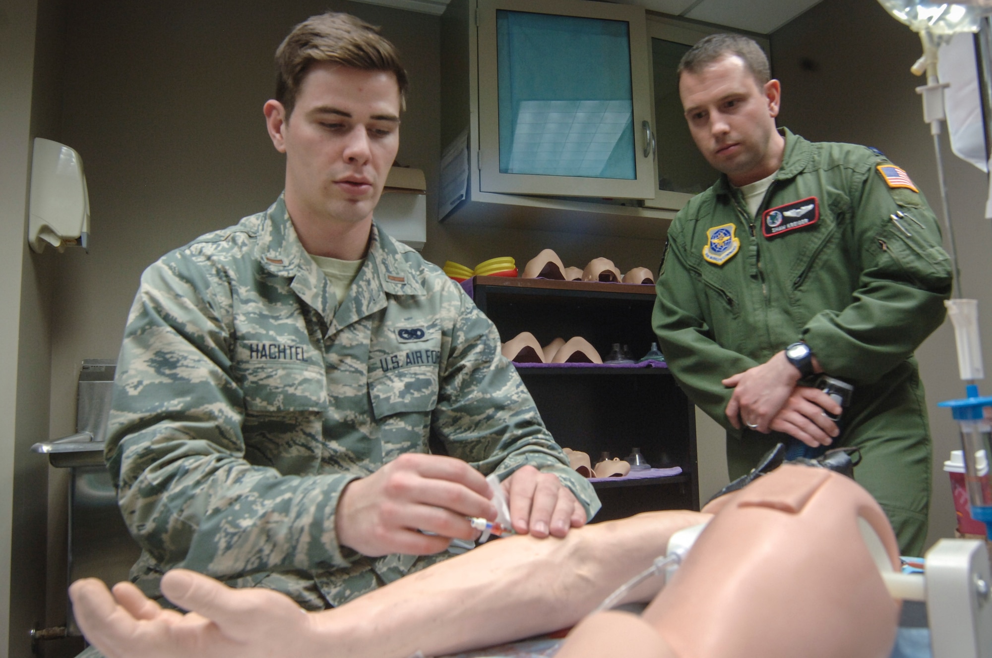 2nd Lt. Adam Hachtel, 92nd Logistics Readiness Group installation deployment officer, practices starting an I.V. in a dummy arm as Capt. Shaw Kreiger, 92nd Air Refueling Squadron KC-135 Stratotanker pilot, observes during the CGO Mission Orientation Brief March 24, 2015, at Fairchild Air Force Base, Wash. The CGO MOB allowed a group of 15 CGOs to spend a week touring the various units of the 92nd ARW.  (U.S. Air Force photo/2nd Lt. Shelley Gregory) 
