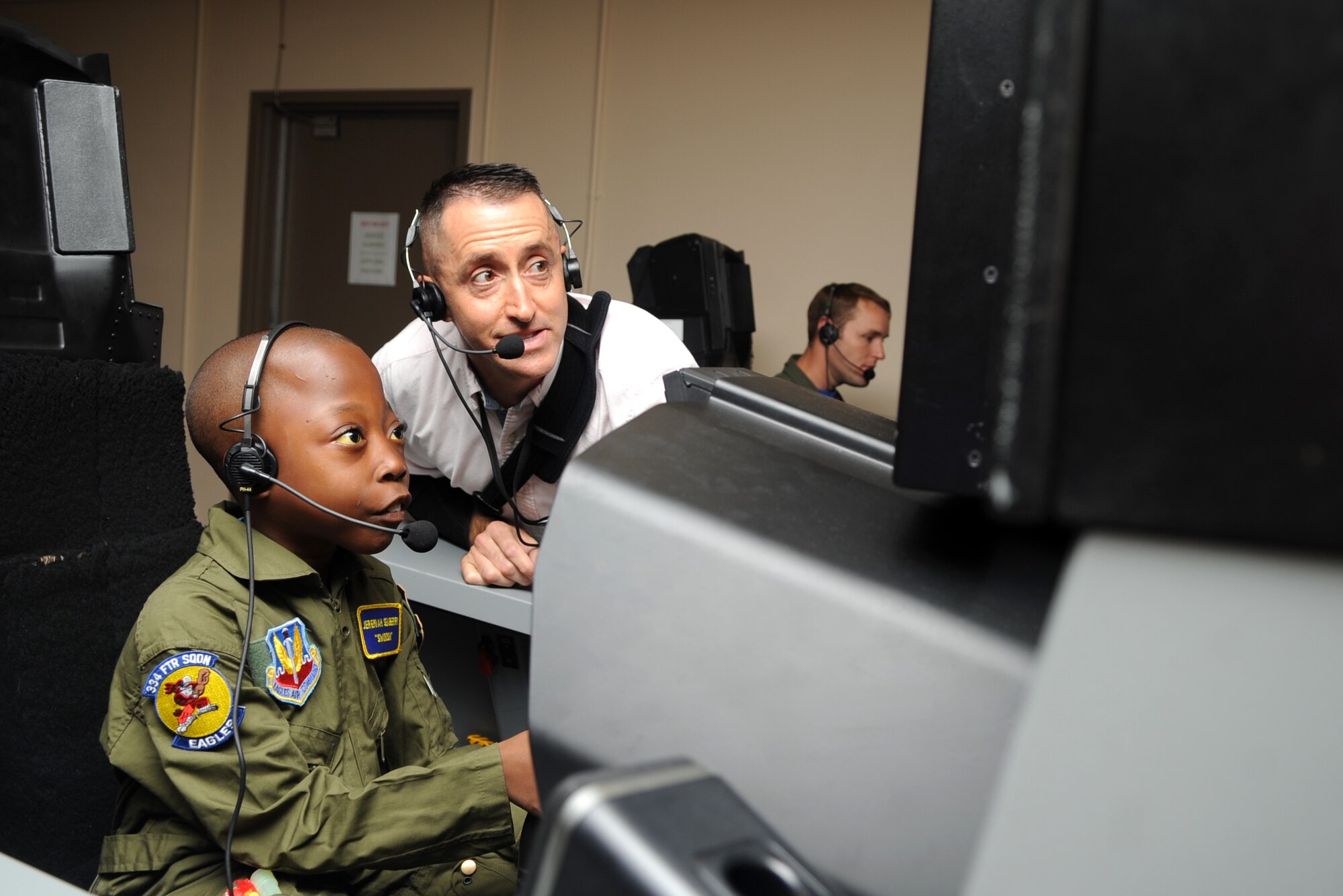 Dan Bayer, Boeing Aerospace representative, helps Jeremiah Seaberry, 334th Fighter Squadron pilot for a day, fly an F-15E Strike Eagle simulator with Capt. Adam Luber, 334th FS pilot, during a 4th Fighter Wing Pilot for a Day event, April 3, 2015, at Seymour Johnson Air Force Base, North Carolina. Luber manned the weapons systems officer position while Jeremiah “flew,” and was thrilled at how well Jeremiah performed. (U.S. Air Force photo/Senior Airman Ashley J. Thum)