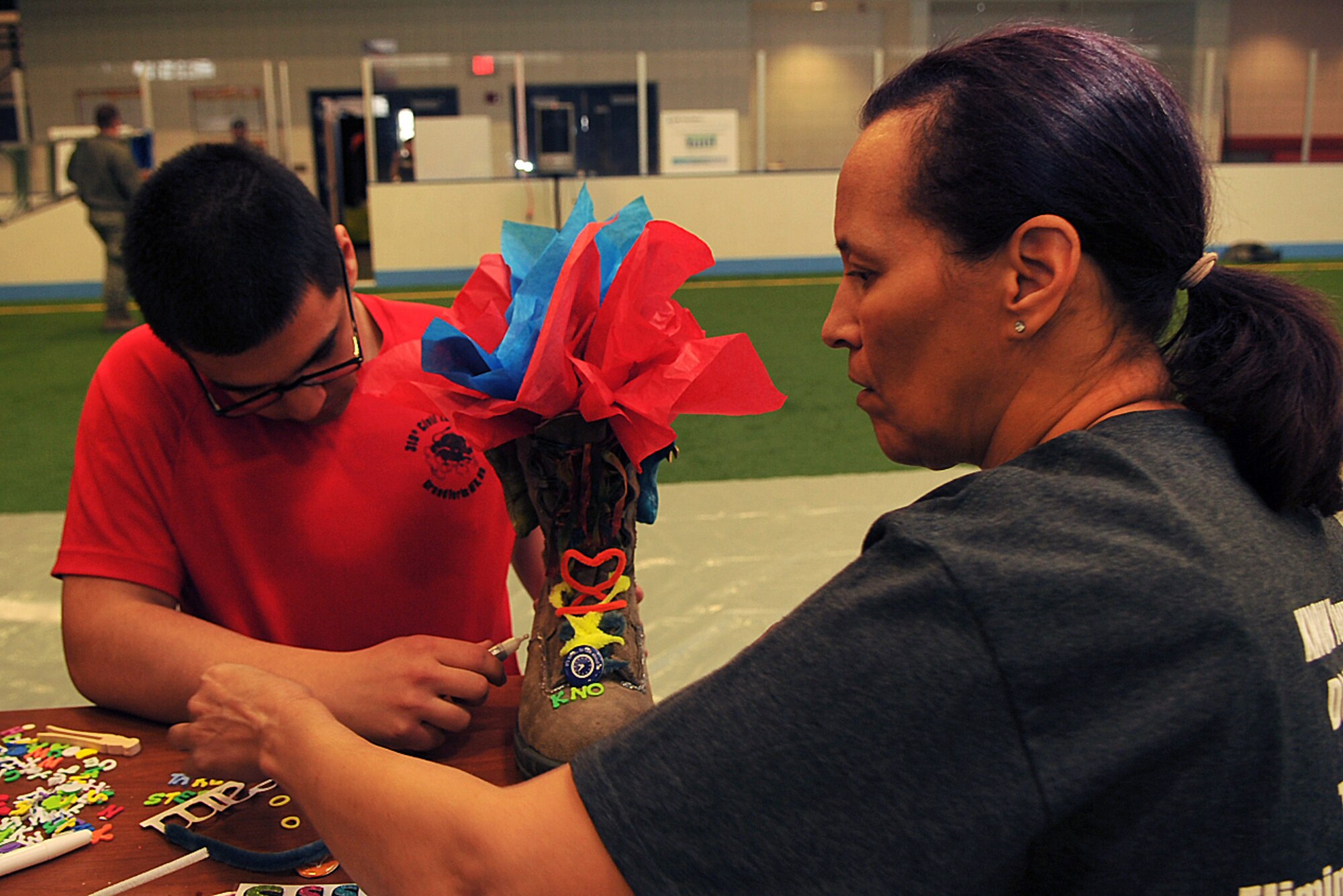 Airman 1st Class Joshua Guting, 319th Civil Engineer Squadron pest management journeyman, and Sonia Brumskill, 319th CES  service contract evaluator, work together to complete their team’s Sexual Assault and Response boot during the Sexual Assault Awareness and Prevention Day of Action boot decorating contest on Grand Forks Air Force Base, N.D., April 7, 2015. Participants in the event were given one pair of boots to decorate: one to represent their squadron and the other to represent Sexual Assault Prevention and Response. (U.S. Air Force photo/Airman 1st Class Bonnie Grantham/released)