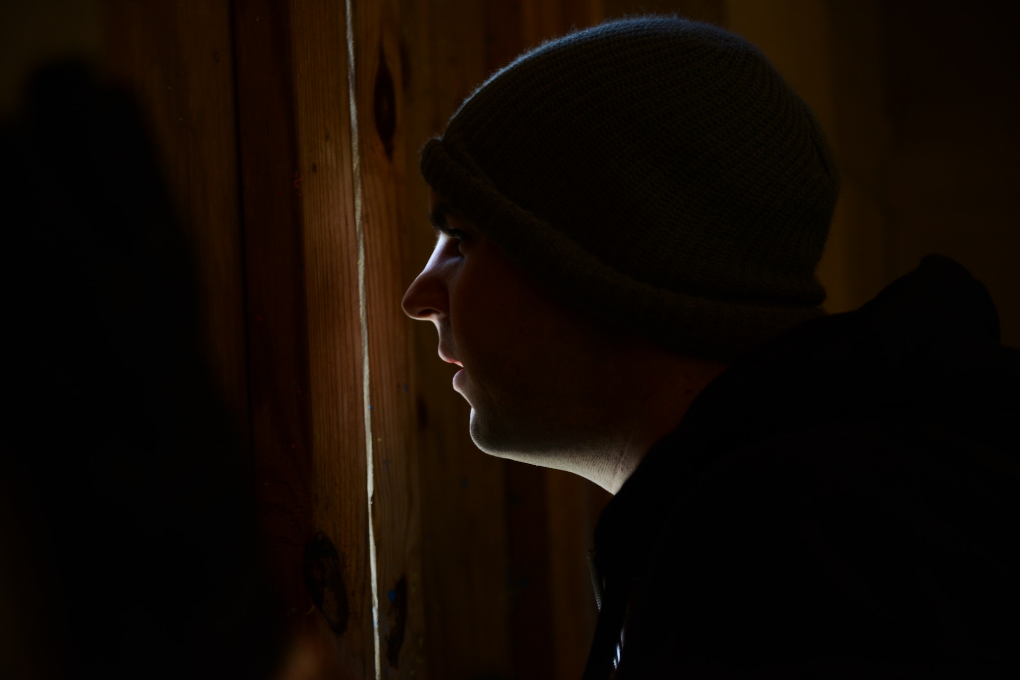 Senior Airman Adam Kwietniak, 6th Airlift Squadron loadmaster, peers through a hole in the wall during a Survival, Evasion, Resistance and Escape exercise on Joint Base McGuire-Dix-Lakehurst, N.J., March 18, 2015. The exercise consisted of four air crew members evading a reaching an extraction point. (U.S. Air Force photo by Airman 1st Class Joshua King/Released)
