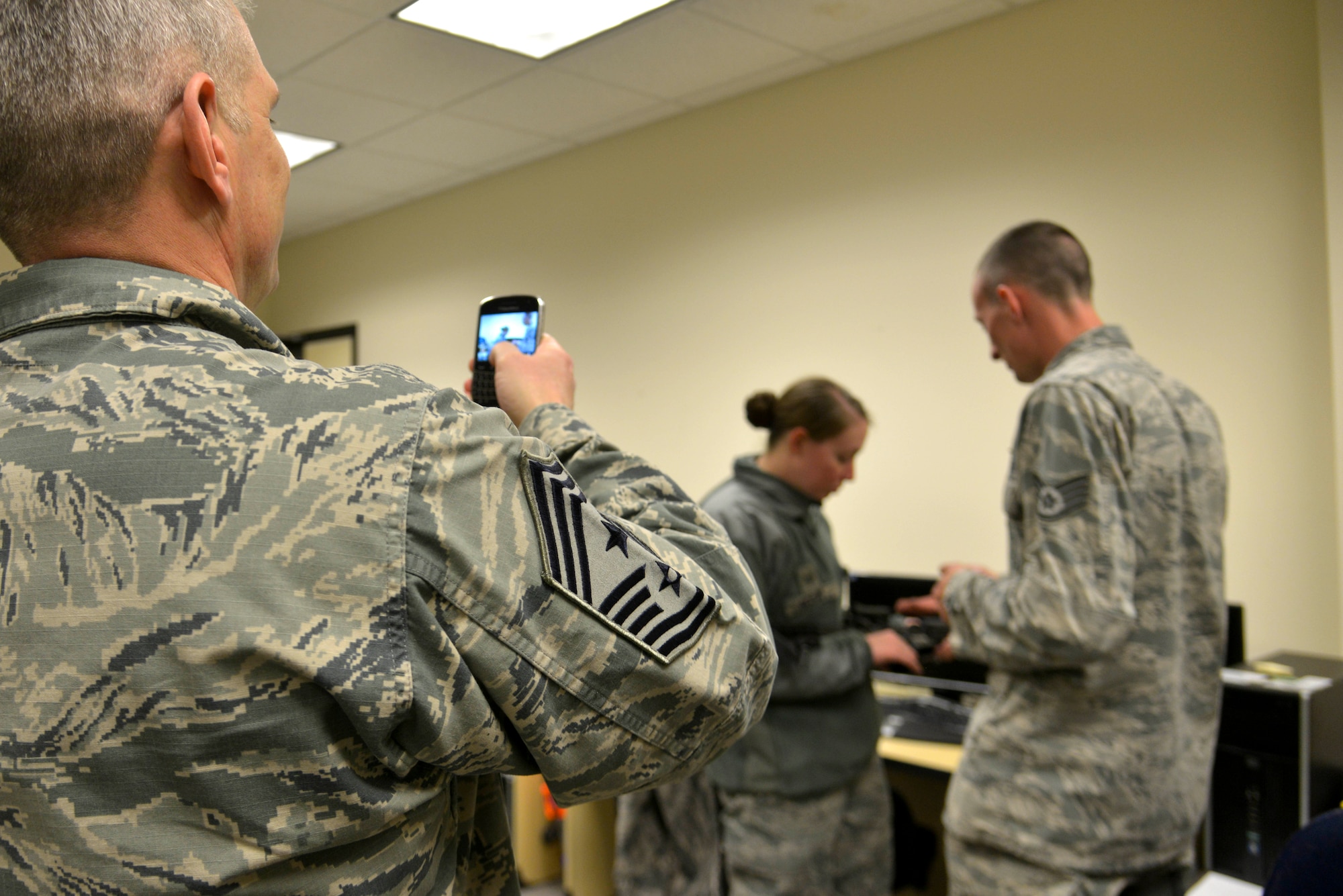 Chief Master Sgt. Christian Pugh, 92nd Air Refueling Wing command chief, takes a photo of Staff Sgt. Tanya Nicolay, 92nd ARW command chief executive assistant, being taught clearing procedures by Staff Sgt. Troy Tulleners, 92nd Security Forces Squadron combat arms instructor, during Operation M4 April 6, 2015, at Fairchild Air Force Base, Wash. Pugh went around the 92nd Communications Squadron building unannounced testing Airmen's knowledge on how to use the weapon making sure they are prepared to go to combat at any time. (U.S. Air Force photo/Senior Airman Janelle Patiño)