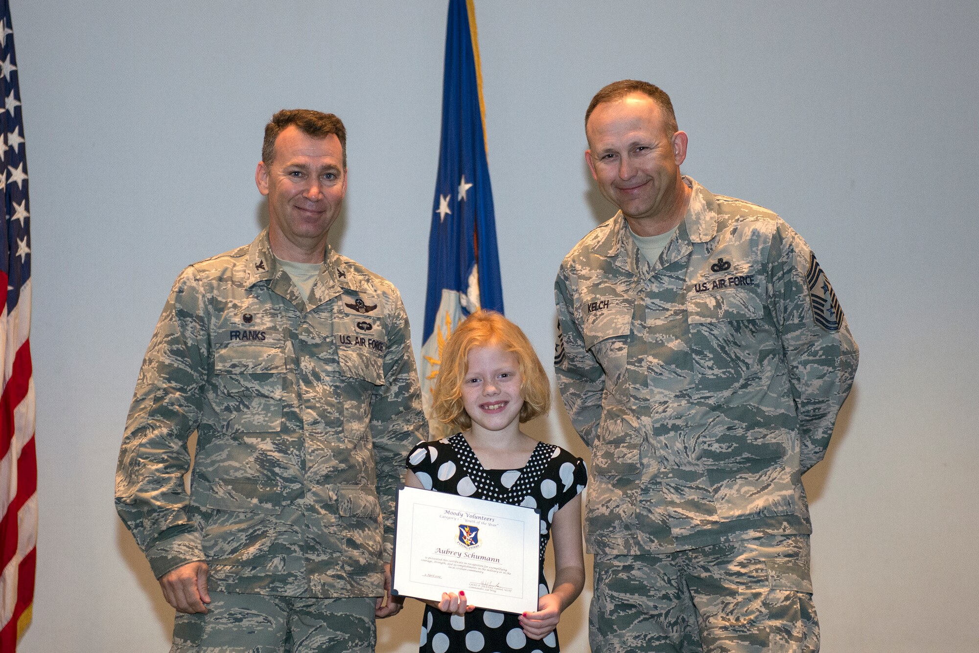 Aubrey Schumann, Category 1 Youth Award winner, poses with U.S. Air Force Col. Chad Franks, 23d Wing commander, left, and Chief Master Sgt. David Kelch, 23d WG command chief, during the Volunteer Recognition Ceremony April 9, 2015, at Moody Air Force Base, Ga. Schumann served the local community by helping the Valdosta-Lowndes Parks and Recreation Authority with the 2nd Annual Stocked Cart Race, which accumulated approximately $1.5K in food donations and $300 in monetary donations provided to the Hungry At Home charity organization. (U.S. Air Force photo by Airman Greg Nash/Released)