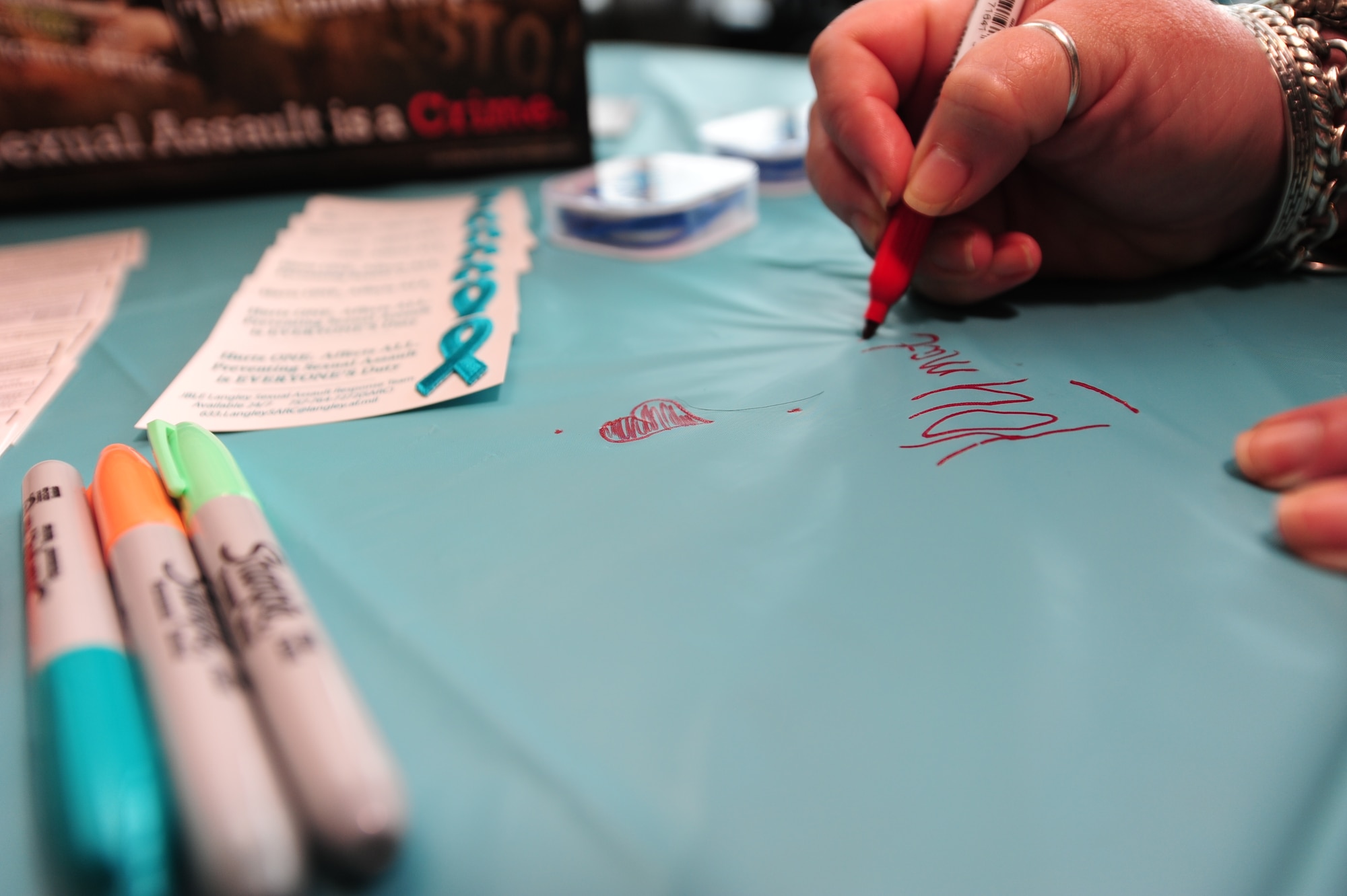 A participant writes words of encouragement to those affected by sexual assault during the Sexual Assault Awareness Fair at the U.S. Air Force Hospital Langley atrium at  Langley Air Force Base, Va., April 8, 2015. The Sexual Assault Prevention and Response team set up the encouragement table and offered facts about sexual assault prevention and response. (U.S. Air Force photo by Staff Sgt. Natasha Stannard/Released) 