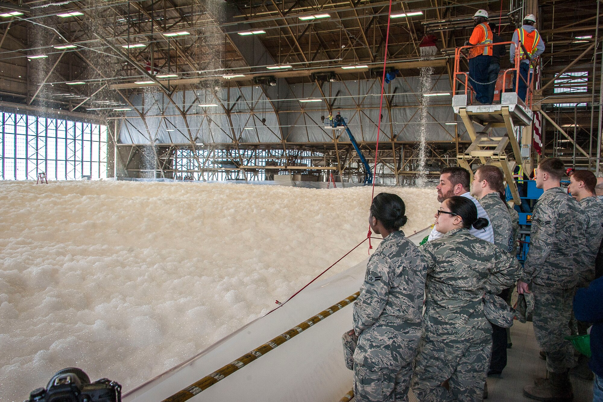 Airmen watch as fire suppression foam engulfs a maintenance hangar testing the installation’s high expansion foam discharge in the repair aircraft maintenance hangar April 8, 2015, at Fairchild Air Force Base, Wash. According to the 92nd Civil Engineer Squadron, the main fire threat is posed by a fuel spill finding an ignition source, leading to a challenging fire. A 50 foot diameter pool of burning jet fuel can produce a heat release rate of nearly 300 megawatts. A few hundred gallons of ignited fuel is enough to destroy just about any facility that is not properly protected. This test proved the installation’s primary maintenance hangar is ready for most situations. (U.S. Air Force photo/Staff Sgt. Benjamin W. Stratton)