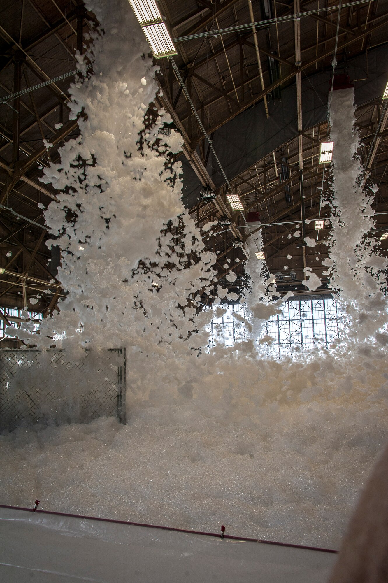 Fire suppression foam engulfs a maintenance hangar as part of a test of the installation’s high expansion foam discharge in the repair aircraft maintenance hangar April 8, 2015, at Fairchild Air Force Base, Wash. The test allowed the installation to assess whether the system was capable of meeting essential milestones required for full certification including covering at least 90 percent of the aircraft’s silhouette and covering the entire hangar floor with at least one meter of foam within four minutes. This test proved the installation’s primary maintenance hangar is ready for most situations. (U.S. Air Force photo/Staff Sgt. Benjamin W. Stratton)